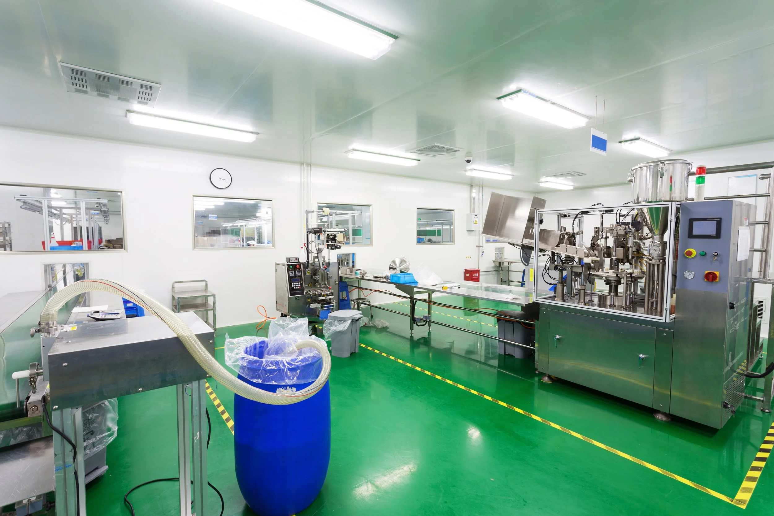 Cleanroom with industrial machinery and equipment, stainless steel tanks, and work tables in a manufacturing or pharmaceutical facility.