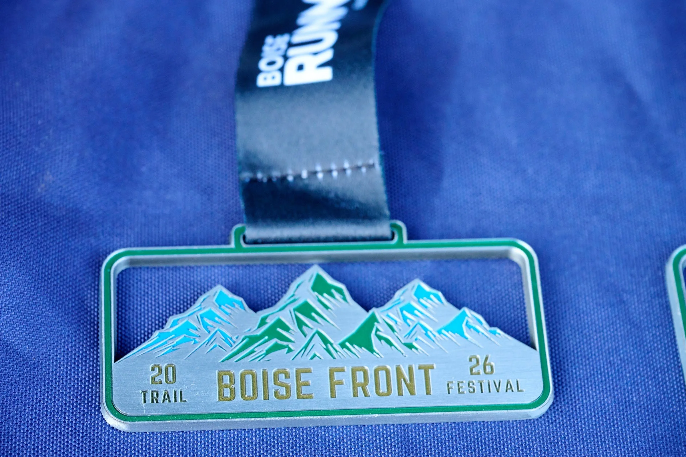 A Boise Front Trail Festival finisher medal with mountains and trees on a blue ribbon
