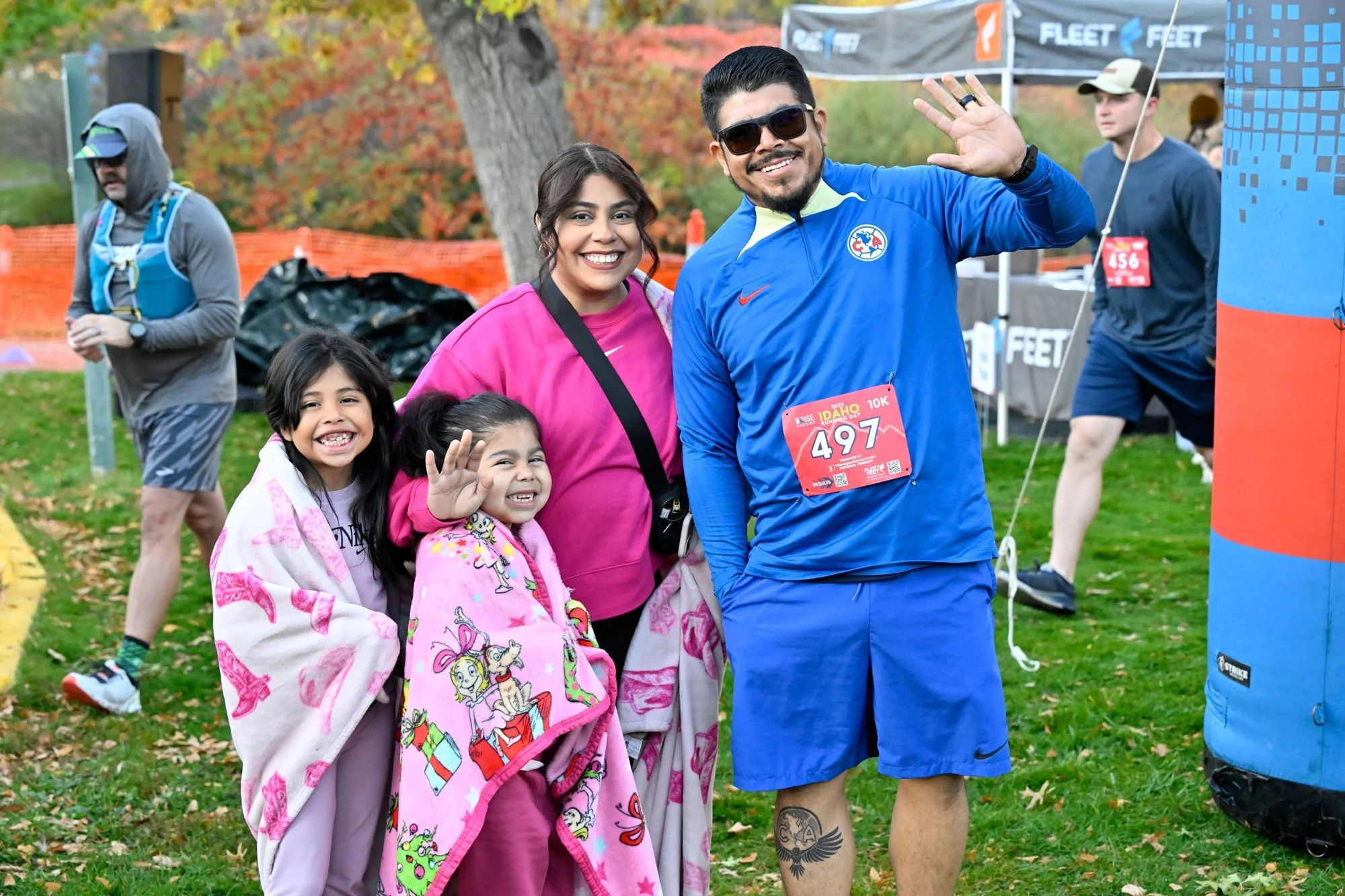 A dad waves while his family, with two little girls wrapped in pink blankets, celebrates at the finish