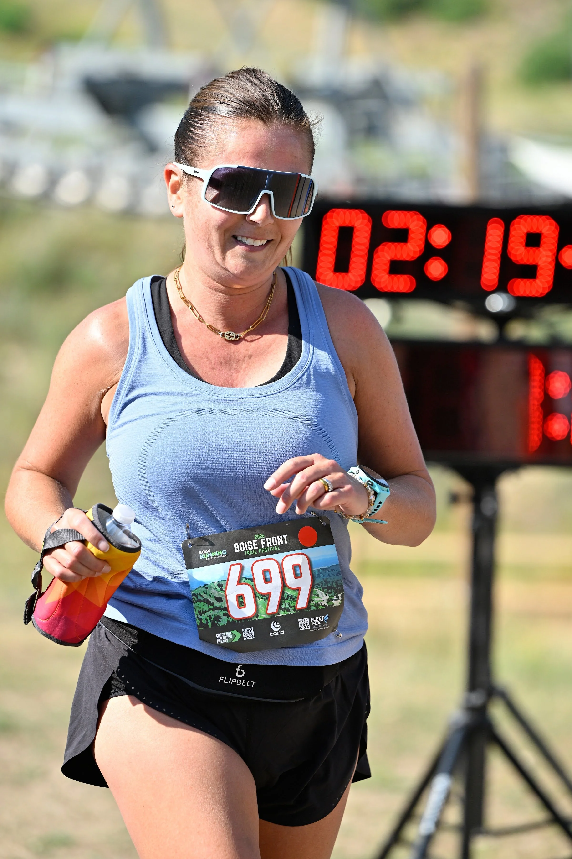 A smiling runner crosses the Boise Front Trail Festival finish line beside the race clock