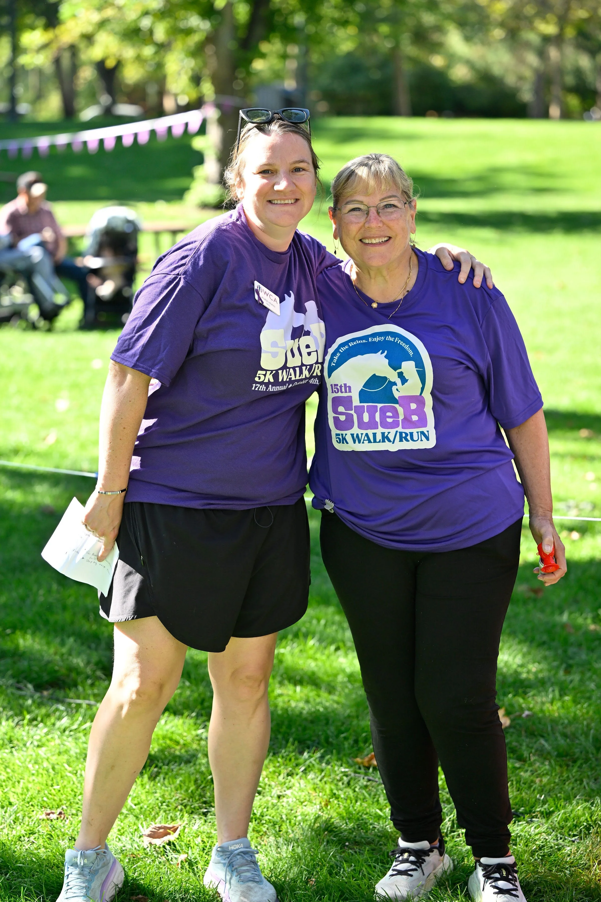 Two women in purple SueB 5K shirts smiling together in Julia Davis Park