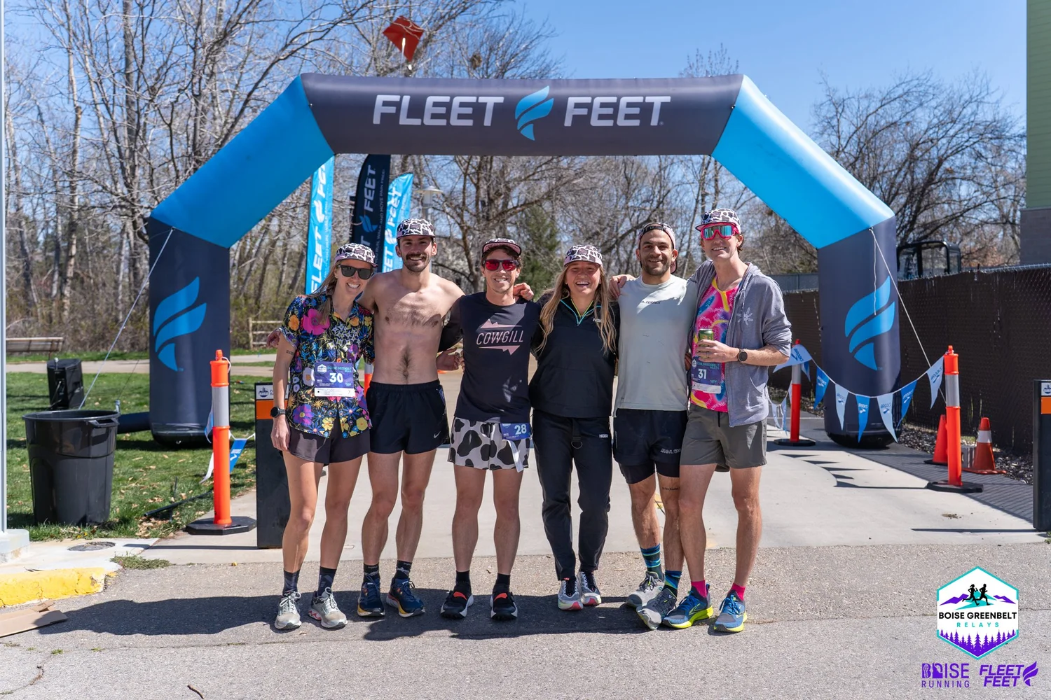 A relay team celebrates together under the Fleet Feet arch