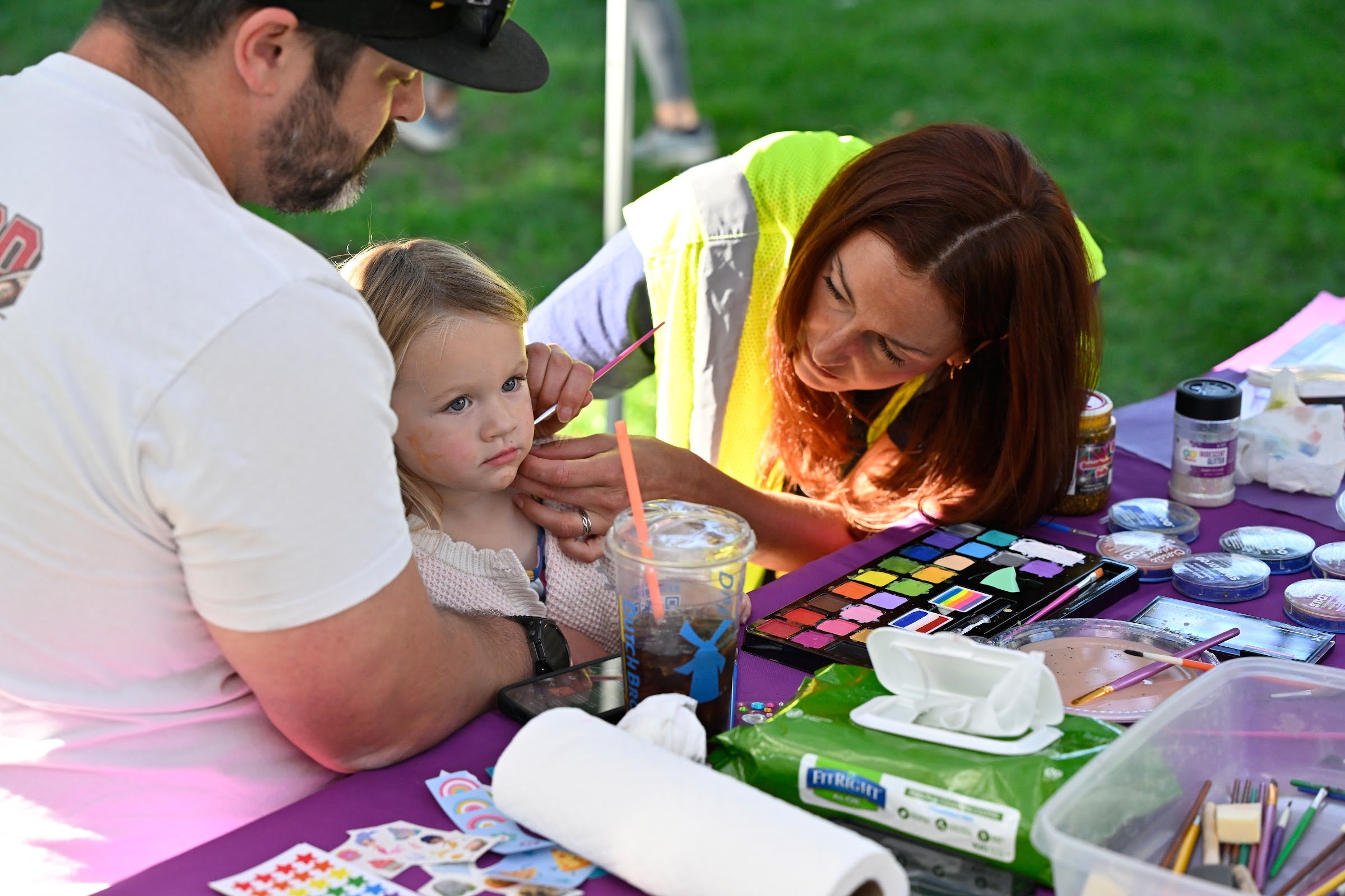 A volunteer painting a young girl's face at the SueB community fair