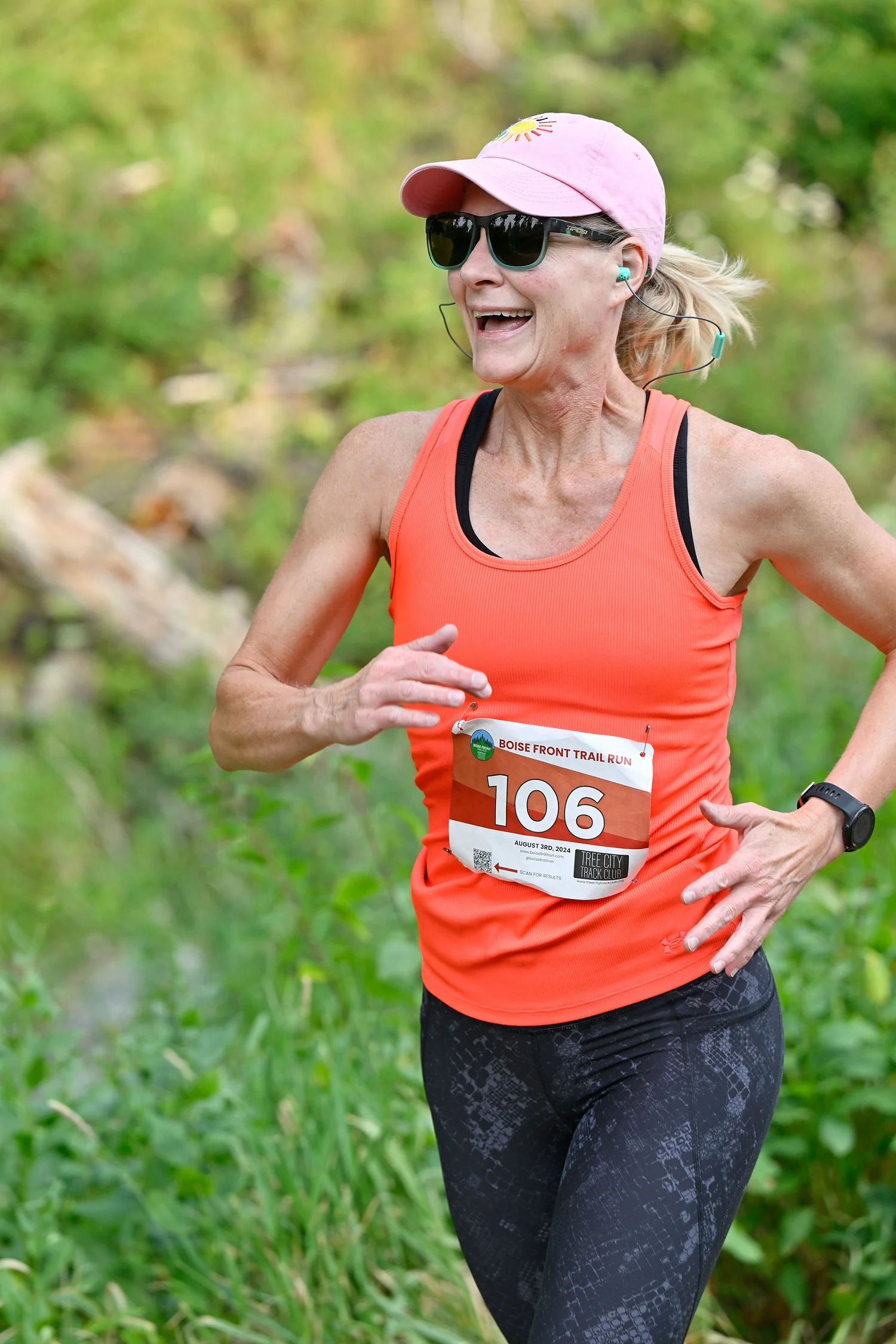 A smiling trail runner in an orange tank on the Boise Front Trail Festival course