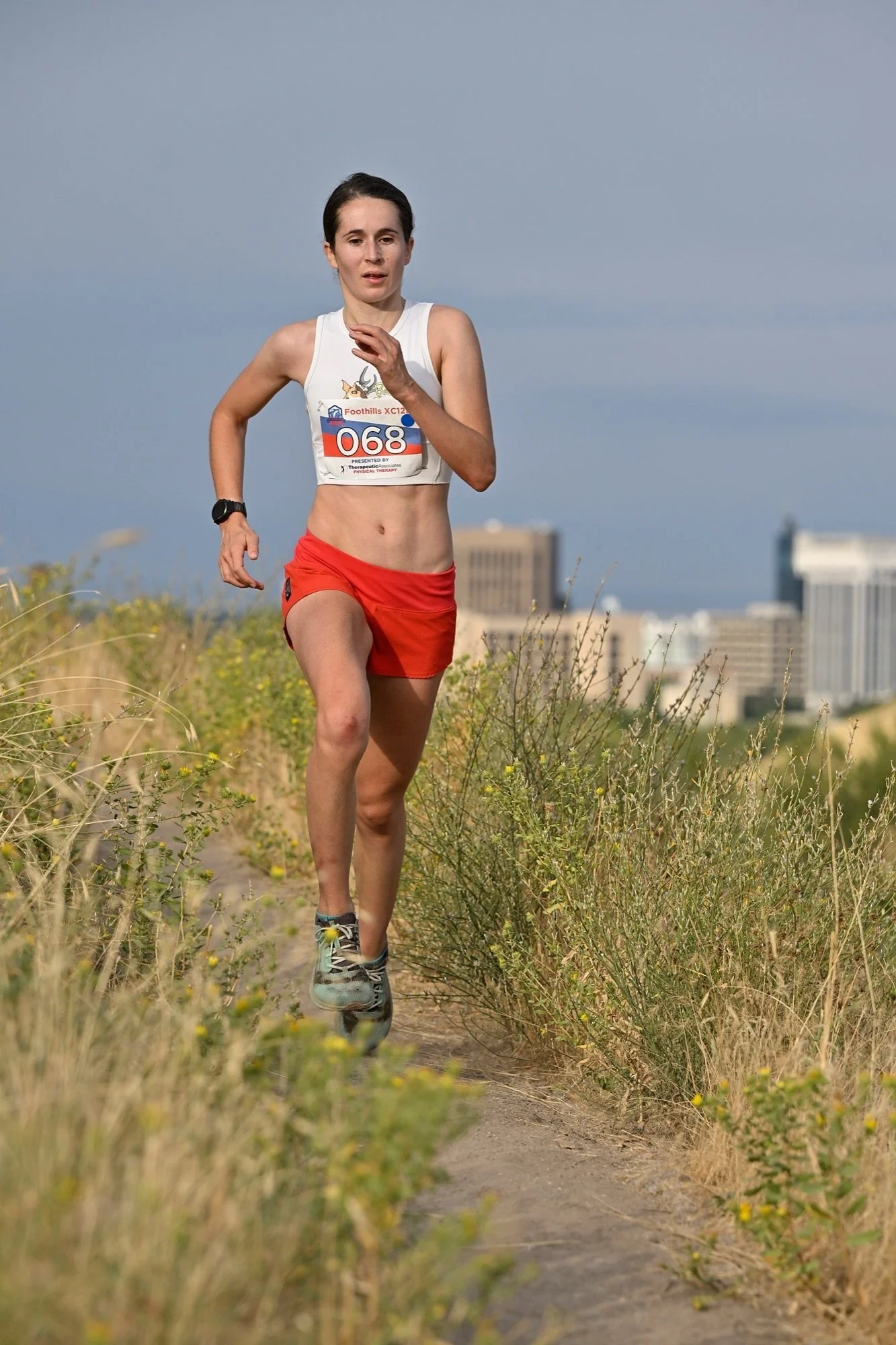 A runner climbs gold grass singletrack with downtown Boise behind her at the Foothills XC12K