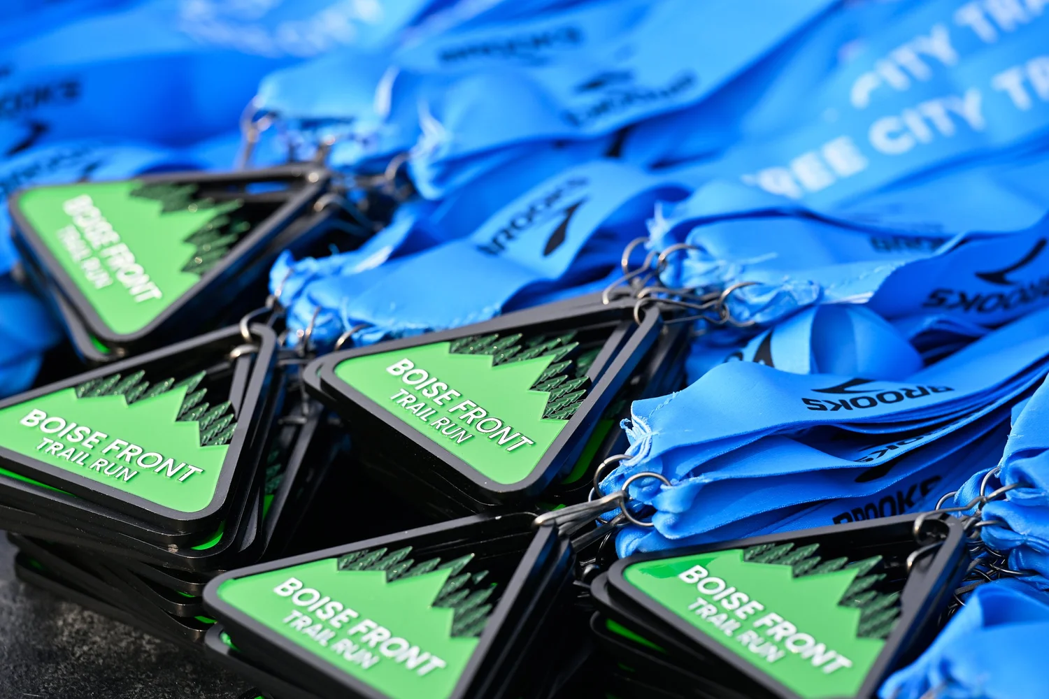 A pile of green Boise Front Trail Festival finisher medals on blue ribbons