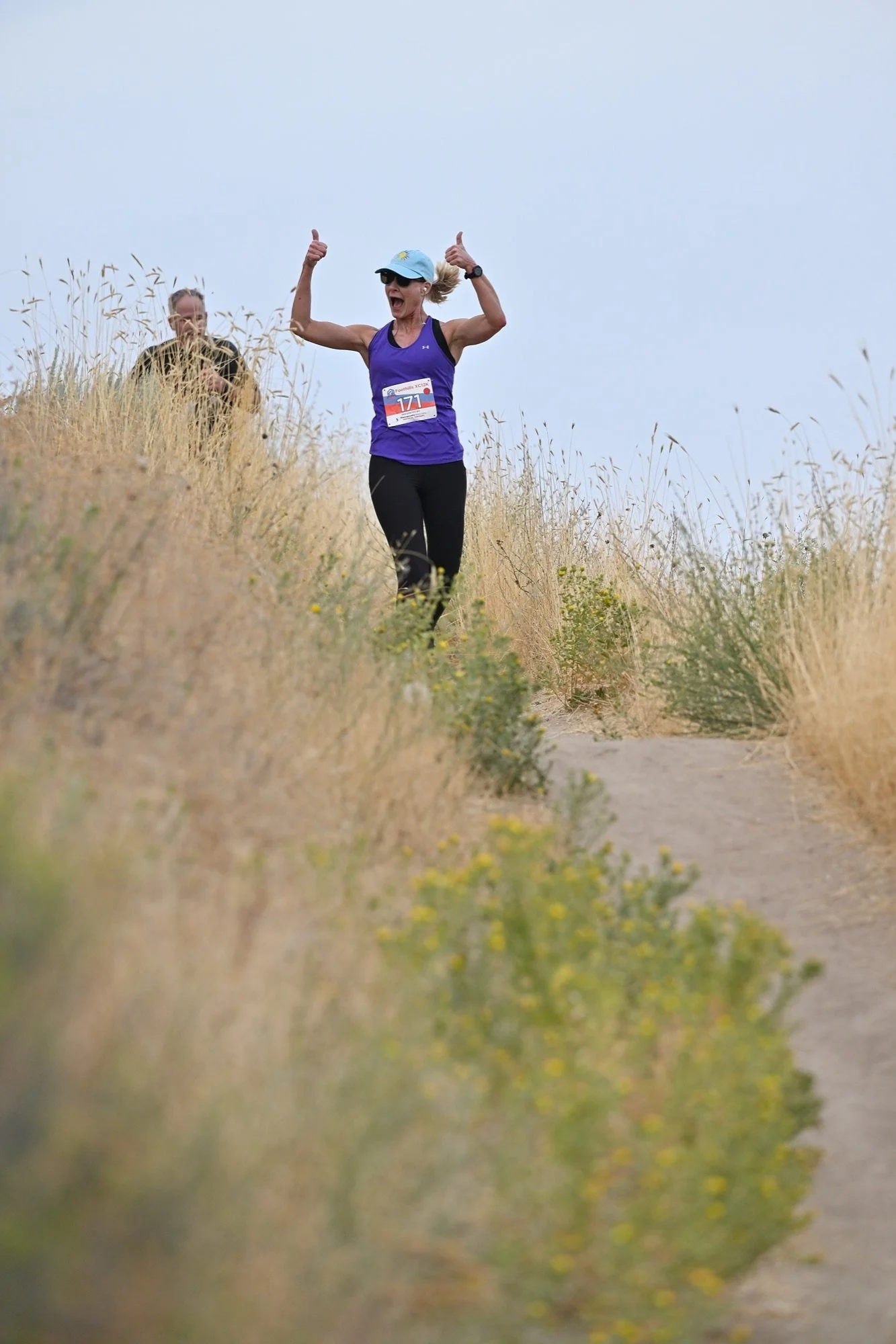 A runner throws both arms up on a gold grass ridge in the Boise Foothills at the XC12K