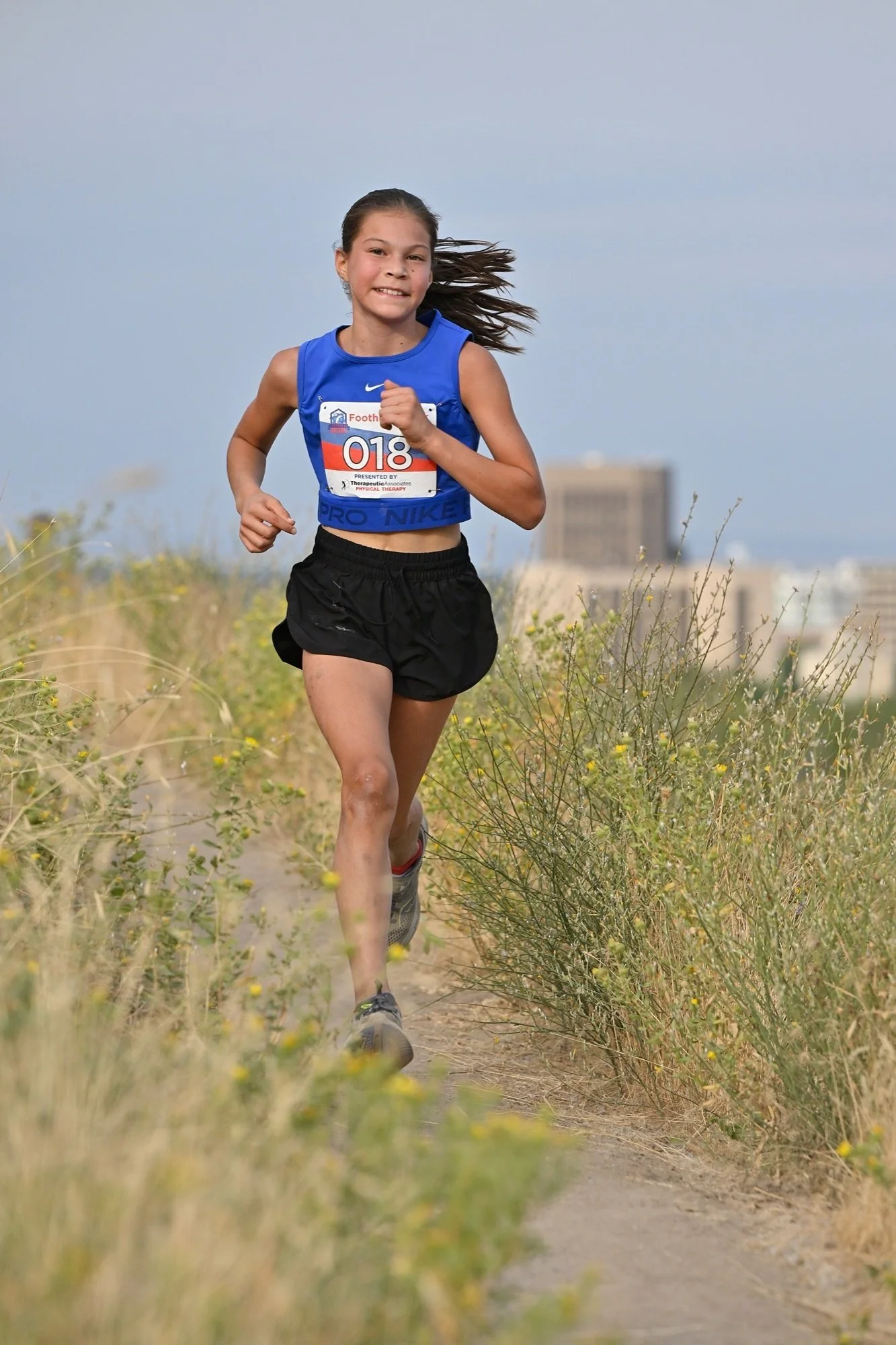 A young runner climbs Foothills singletrack with downtown Boise behind her at the XC12K