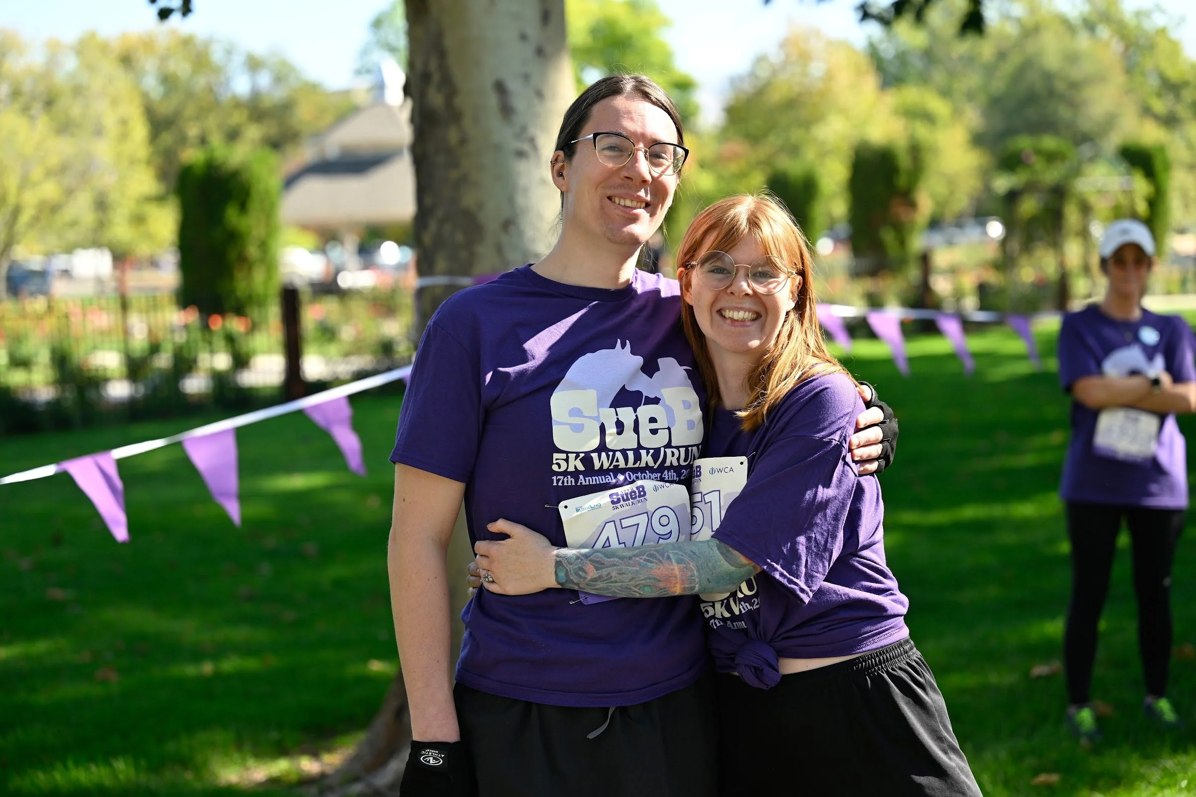 Two friends in purple SueB shirts smiling arm in arm in Julia Davis Park