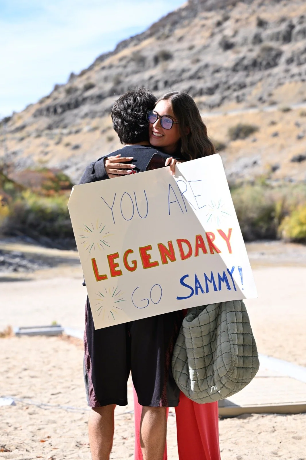 A runner hugs a friend holding a sign that says You Are Legendary at the Sandy Point finish