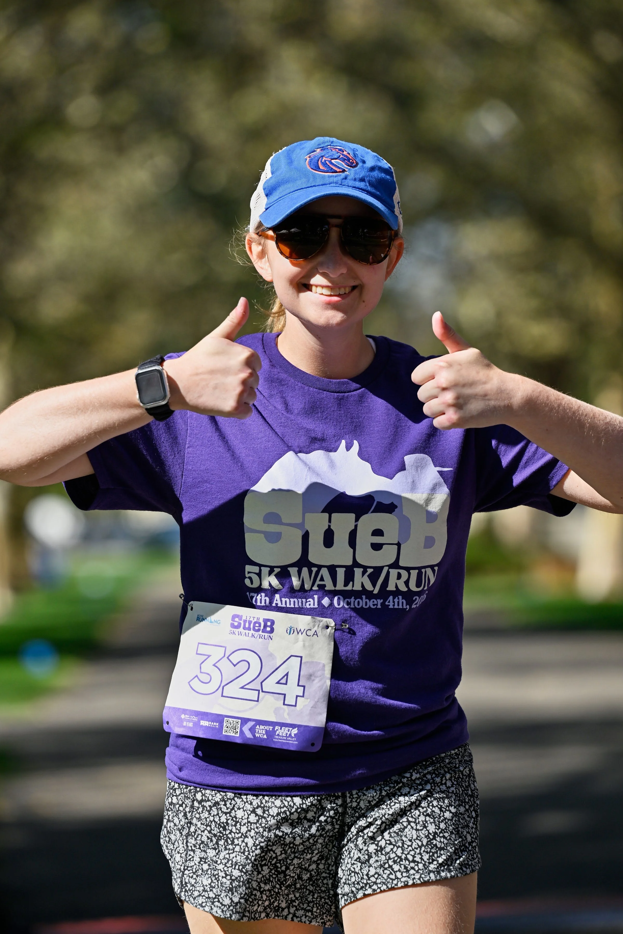 A smiling SueB runner in a purple shirt giving two thumbs up on the course