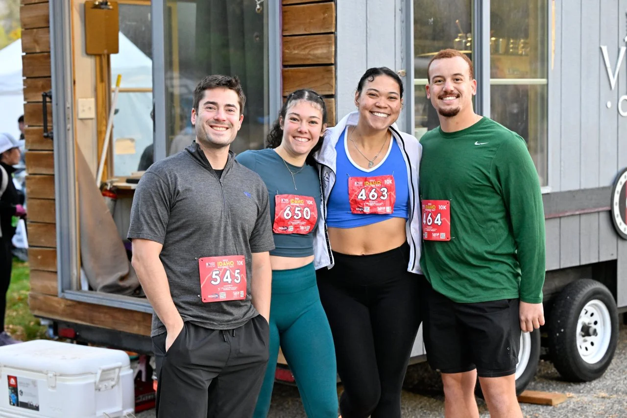 Four smiling finishers with their race bibs after Idaho Running Day