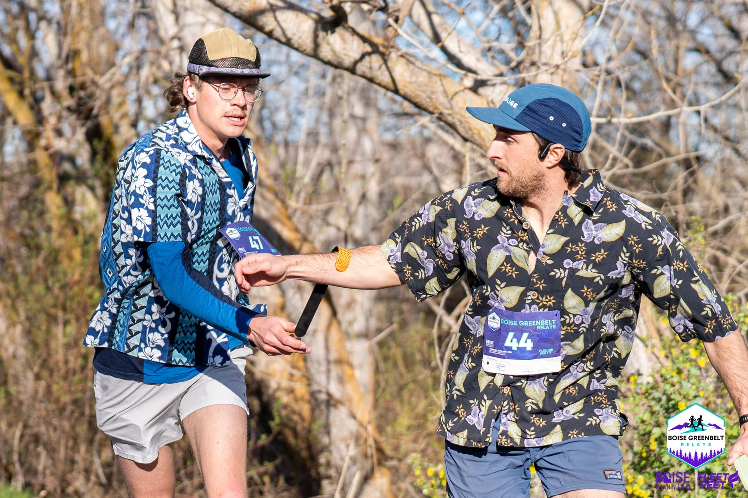Two relay runners in Hawaiian shirts pass the baton on the Boise River Greenbelt