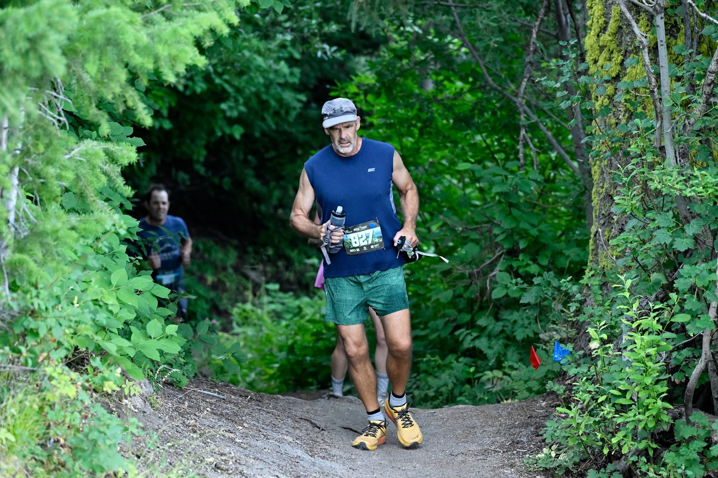 A smiling trail runner in a blue shirt climbs out of the trees on the Boise Front course