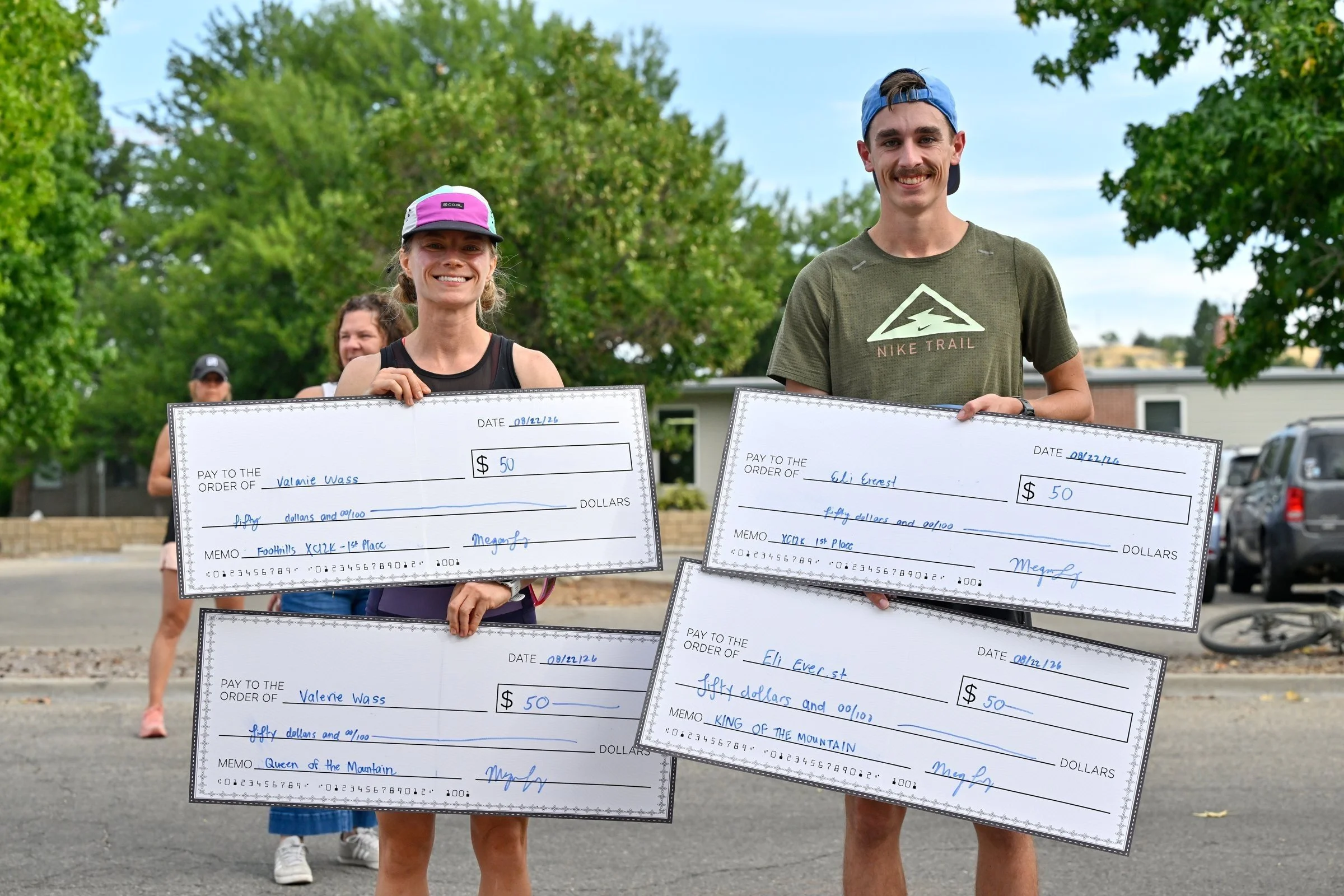 Two 2026 XC12K winners hold up their oversized prize checks at the finish