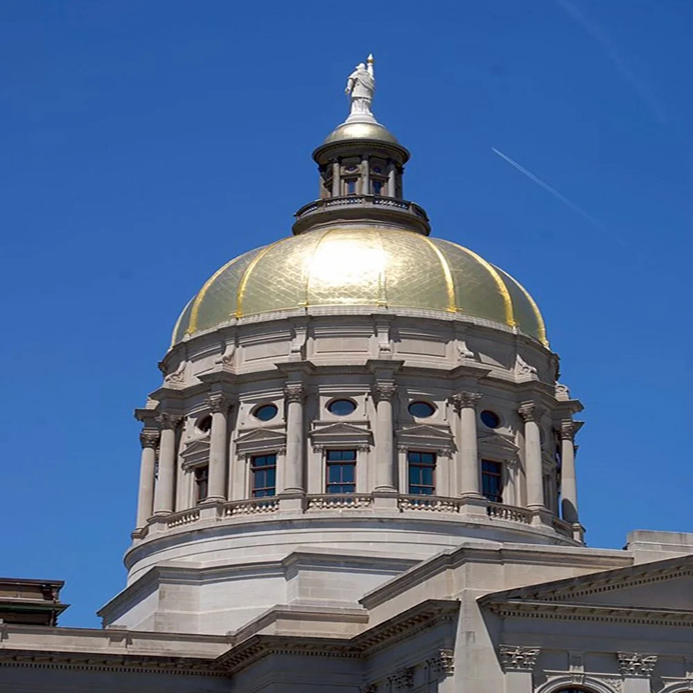 A domed government building with a golden roof and a statue on top, against a bright blue sky.