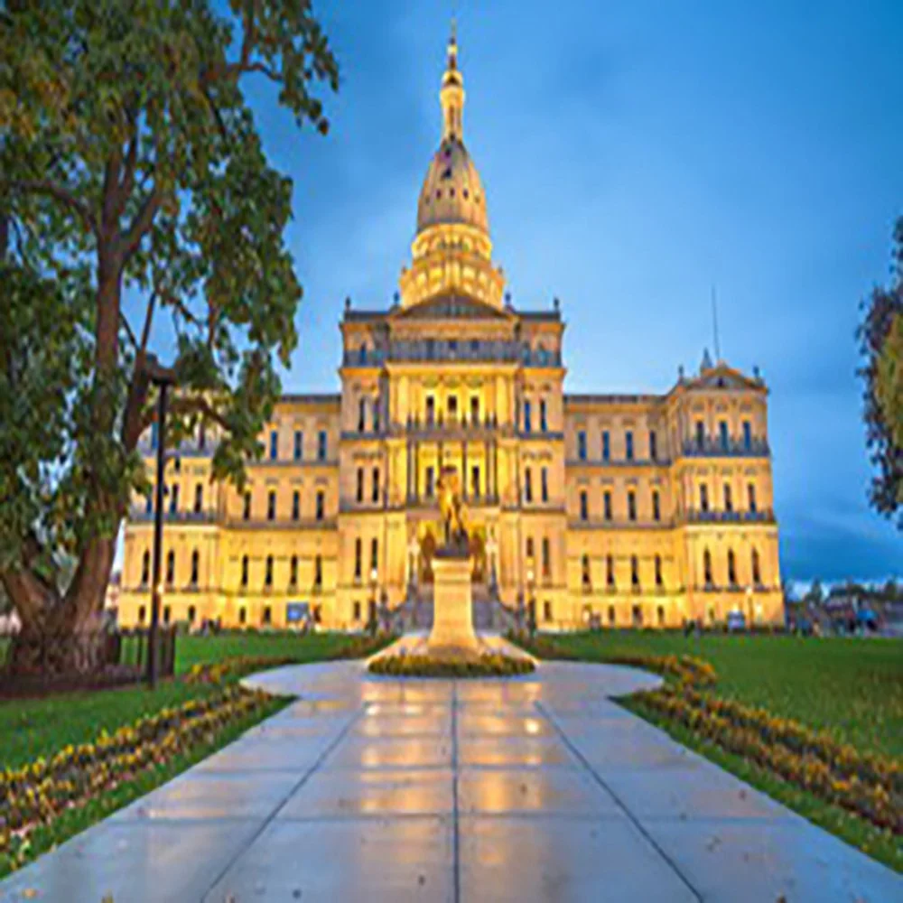 The Illinois State Capitol building illuminated at dusk, with a pathway leading to its entrance and trees on the sides.