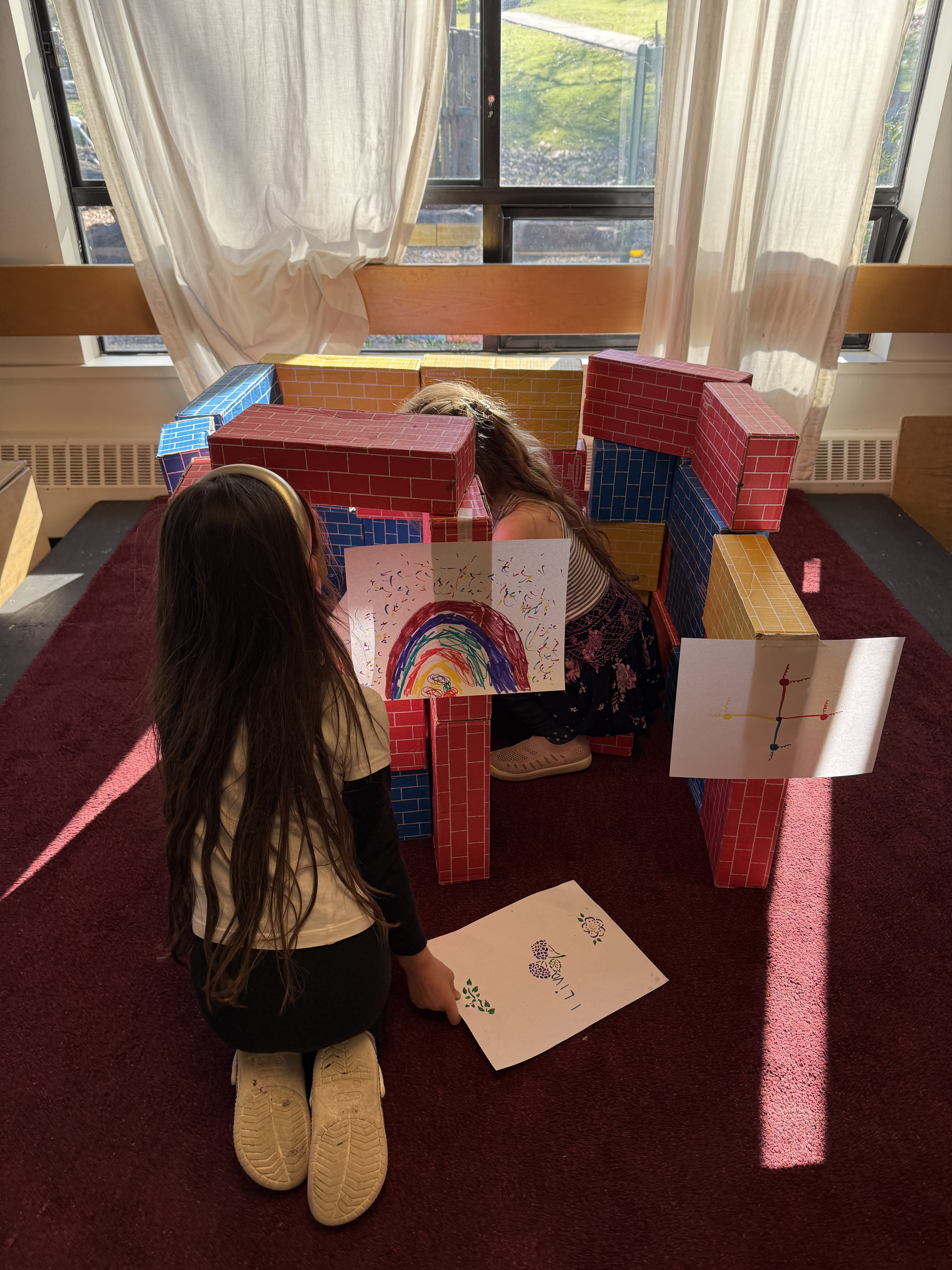 Two young girls are playing with a colorful cardboard block structure.