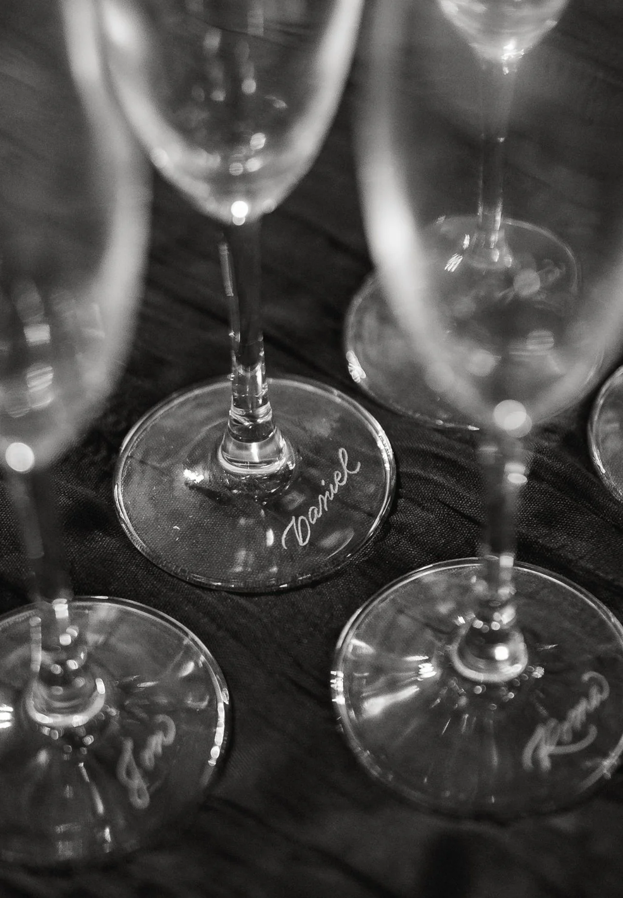 Close-up of empty champagne glasses on a dark surface, with one glass's base inscribed with the name 'Janice'.