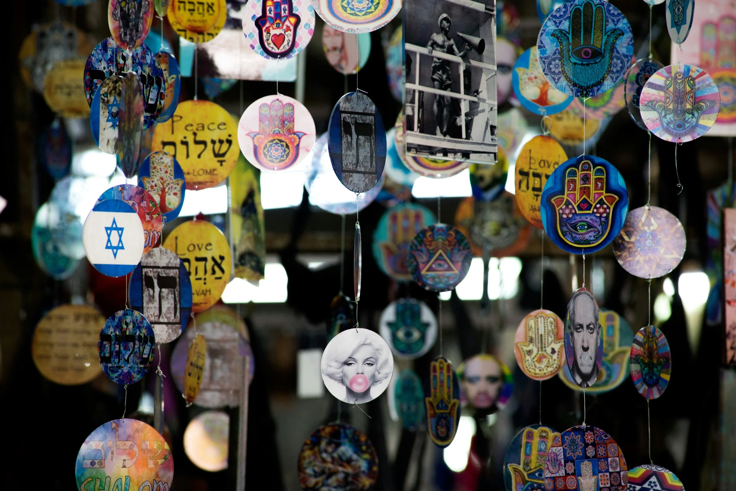 Colorful decorative hanging ornaments featuring symbols, portraits, and words like 'Peace' and 'Love'