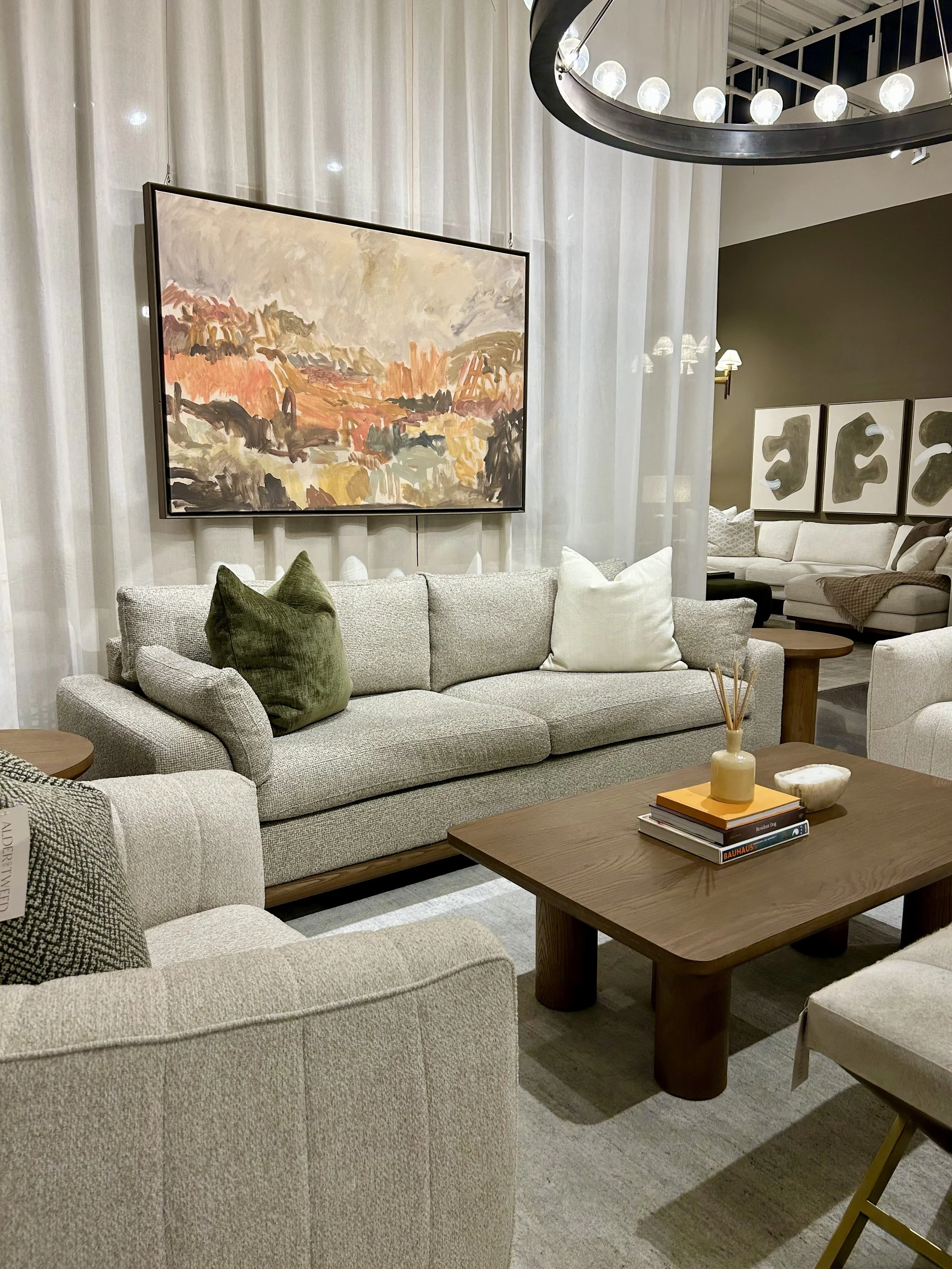 Warm neutral living room display with textured upholstery, wood furniture and earthy green accents at Las Vegas Market.