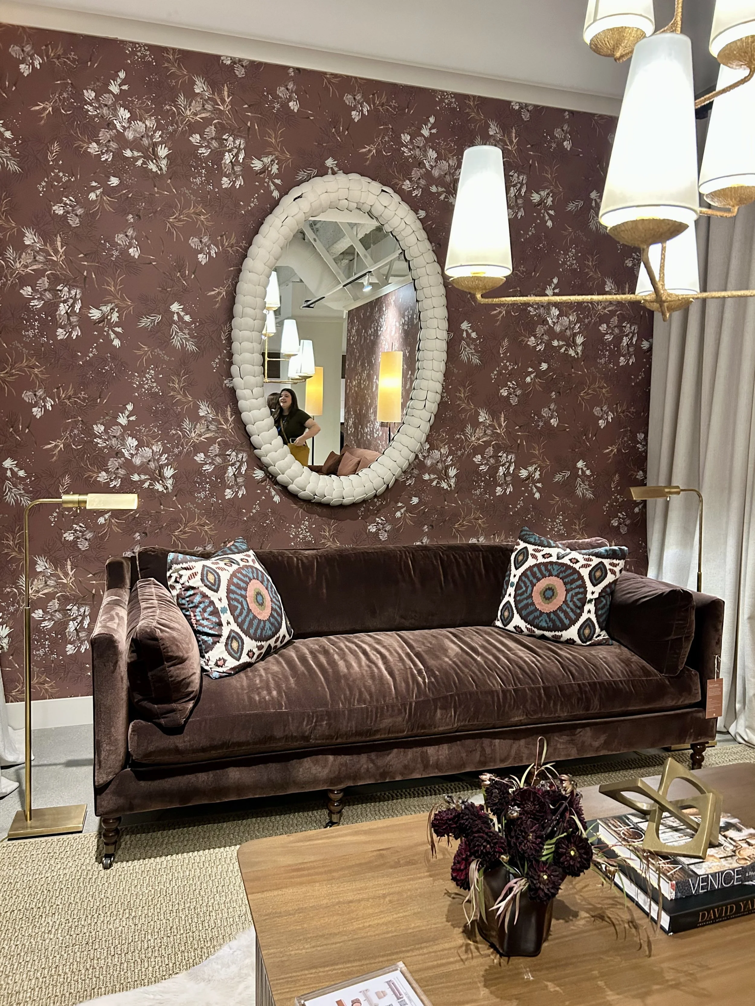 Brown velvet sofa paired with floral wallpaper, patterned pillows and warm brass lighting at Las Vegas Market.