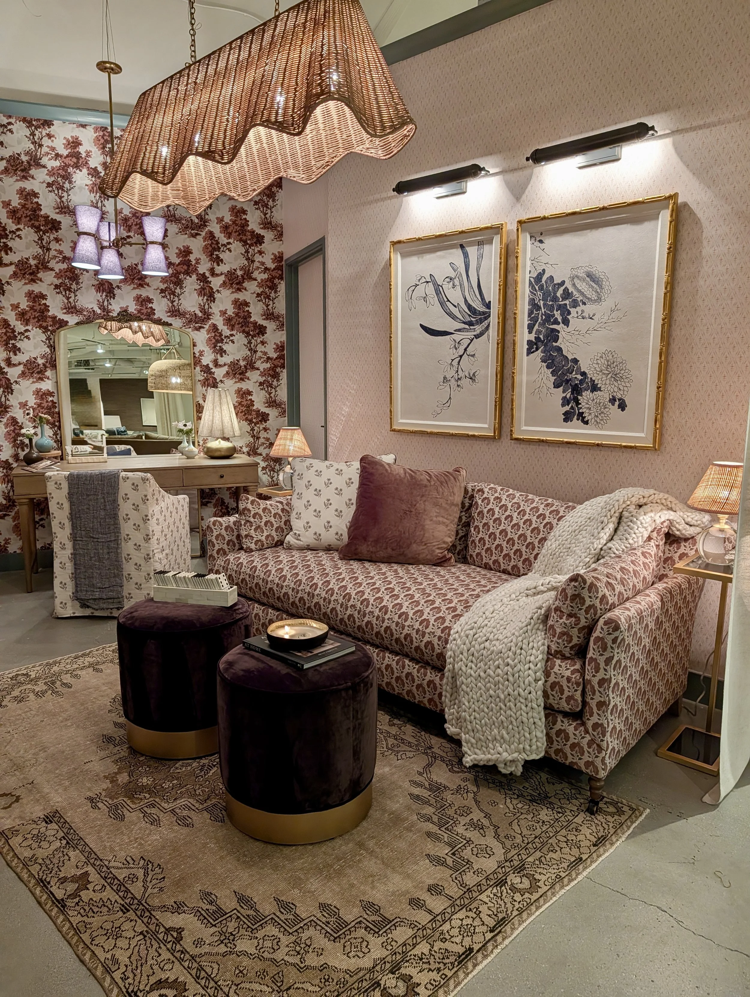 Layered showroom display with patterned upholstery, floral wallpaper, warm wood and woven lighting at Las Vegas Market.