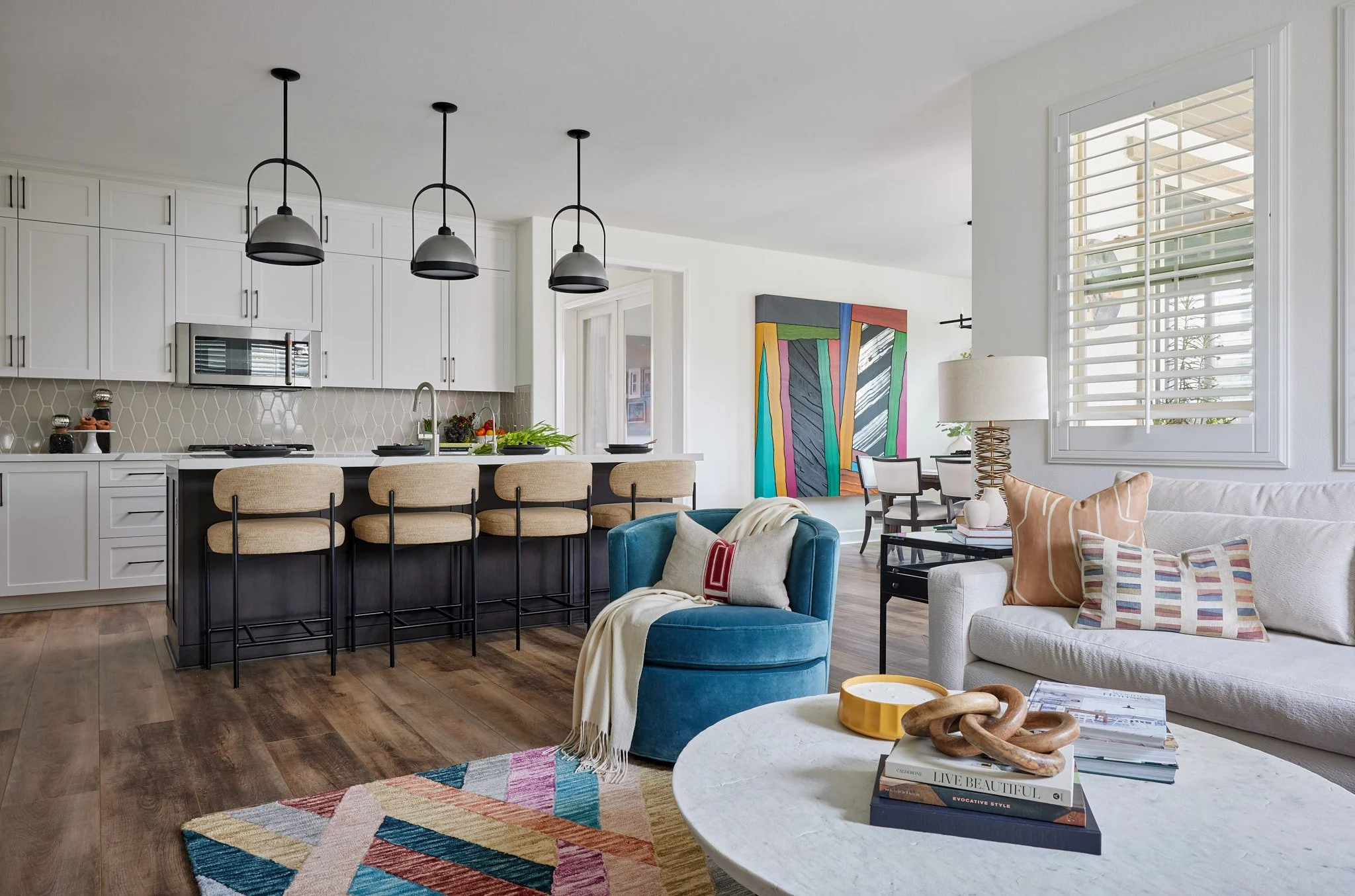 Open kitchen and living room with colorful rug, teal accent chair, and styled coffee table creating a layered interior design look.