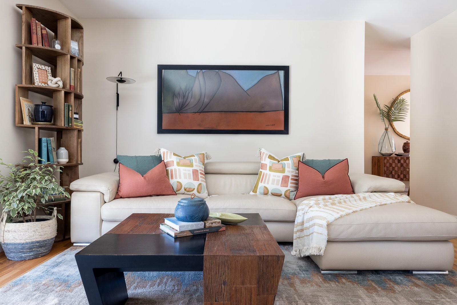 Living room with styled wood bookshelf, neutral sectional sofa, and layered coffee tables highlighting collected objects and books.