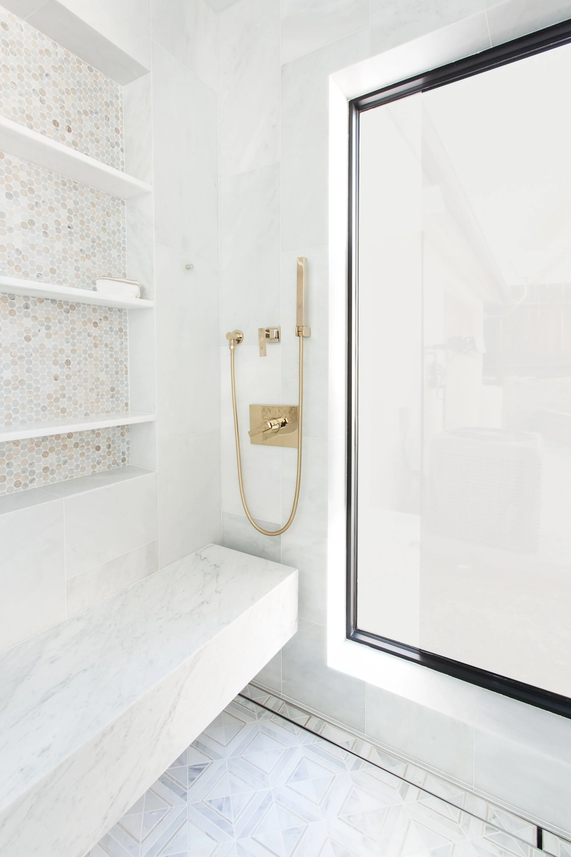 Accessible walk-in shower with built-in marble bench, handheld shower fixture, and recessed shelving for aging-in-place comfort and functionality.