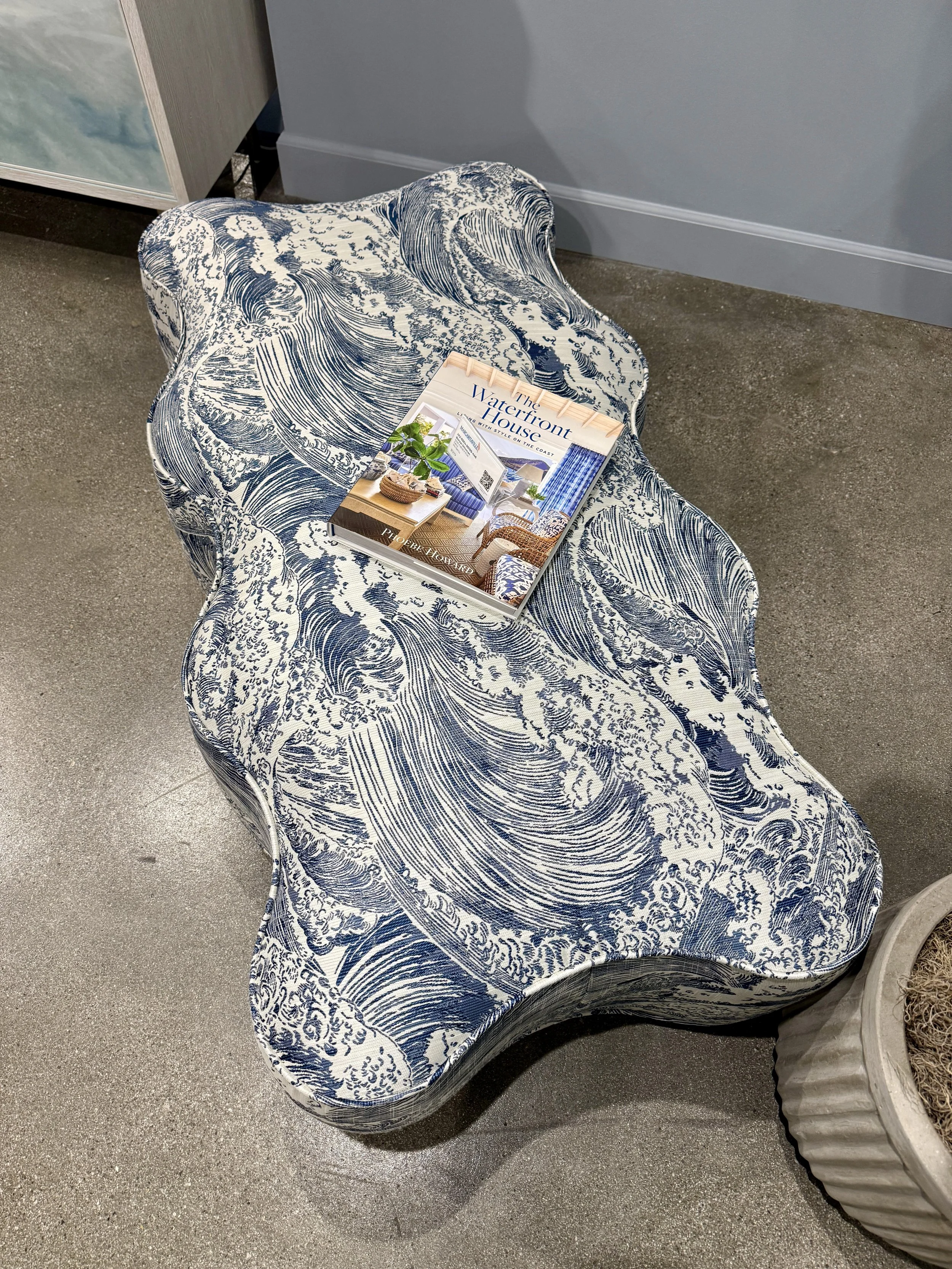 Blue and white wave-patterned upholstered ottoman with a sculptural wavy edge at Las Vegas Market.