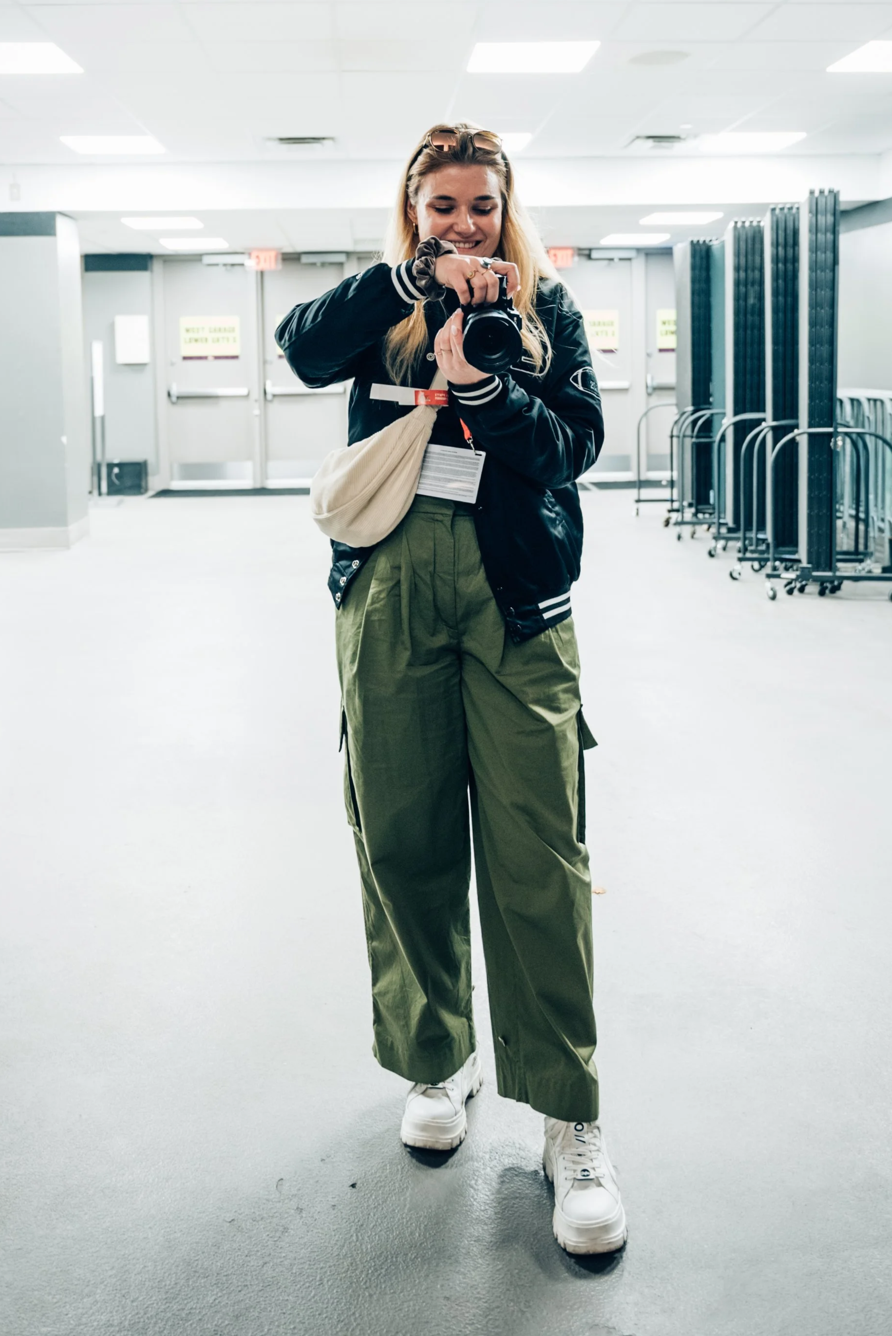 Junge Frau bei der NFL Experience in Las Vegas im Allegiant Stadium, trägt eine schwarze Jacke, grüne Klamotten, weiße Schuhe und hält eine Fotokamera.