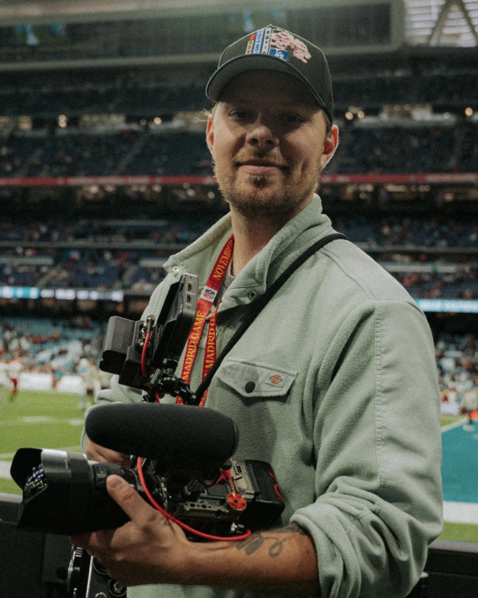 Ein Mann mit Baseballkappe, der eine Kamera bei einem Sportereignis im Stadion hält.