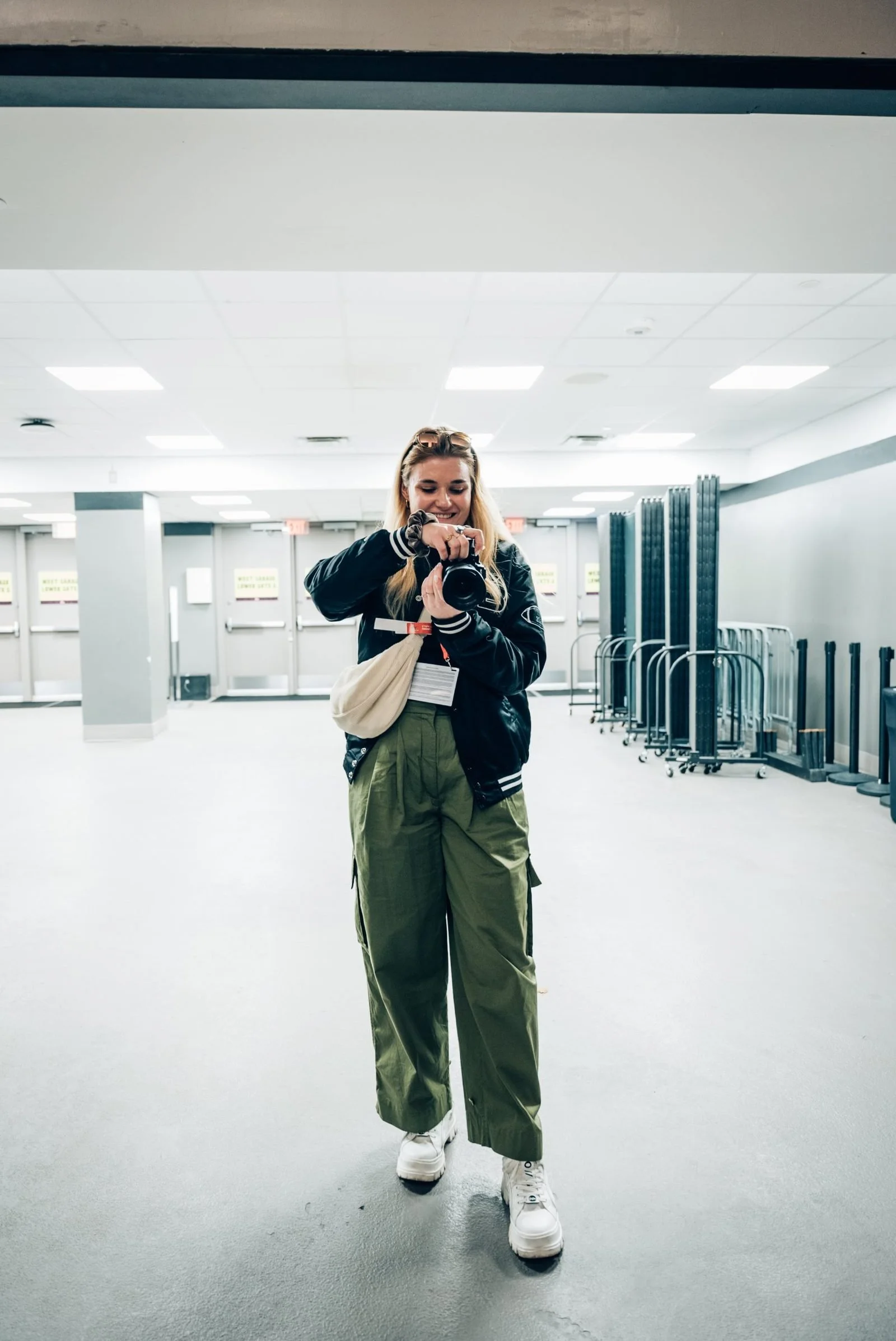 Junge Frau bei der NFL Experience in Las Vegas im Allegiant Stadium, trägt eine schwarze Jacke, grüne Klamotten, weiße Schuhe und hält eine Fotokamera.
