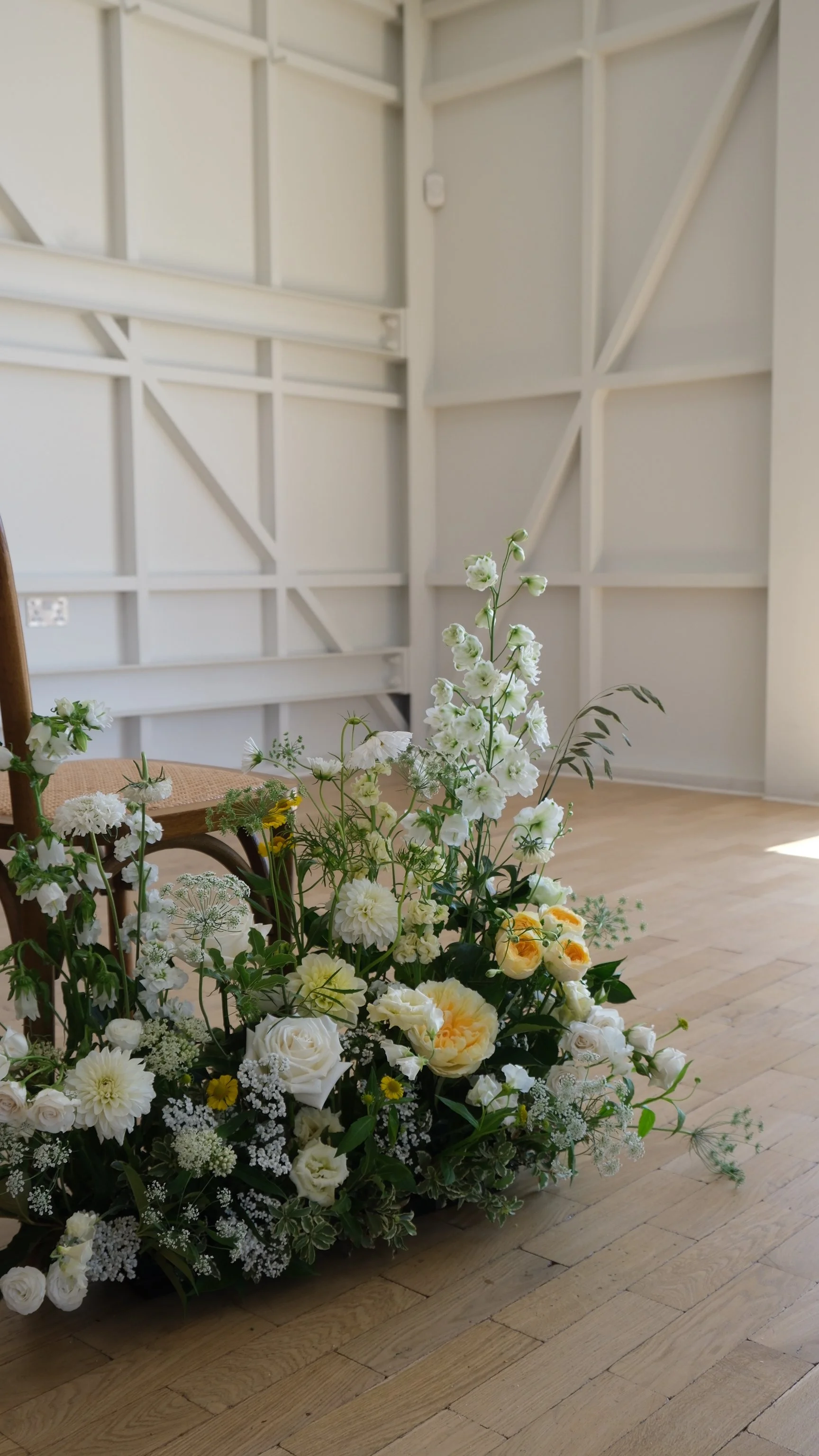 A large arrangement of white and yellow flowers on a wooden floor in a bright room with white paneled walls.
