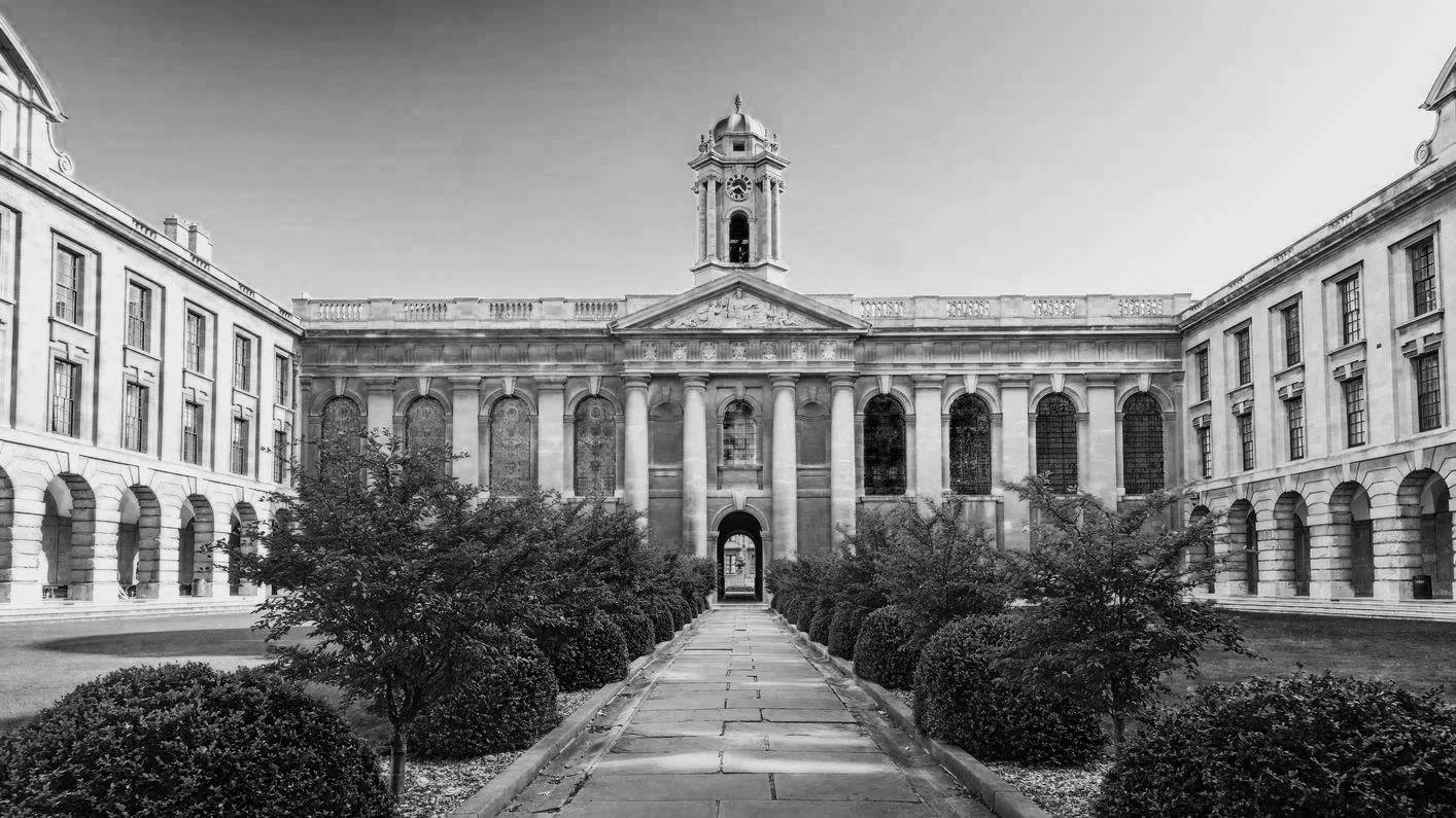 Black and white photograph of an elegant neoclassical building with a central tower and arched windows, surrounded by symmetrical gardens and shrubbery.