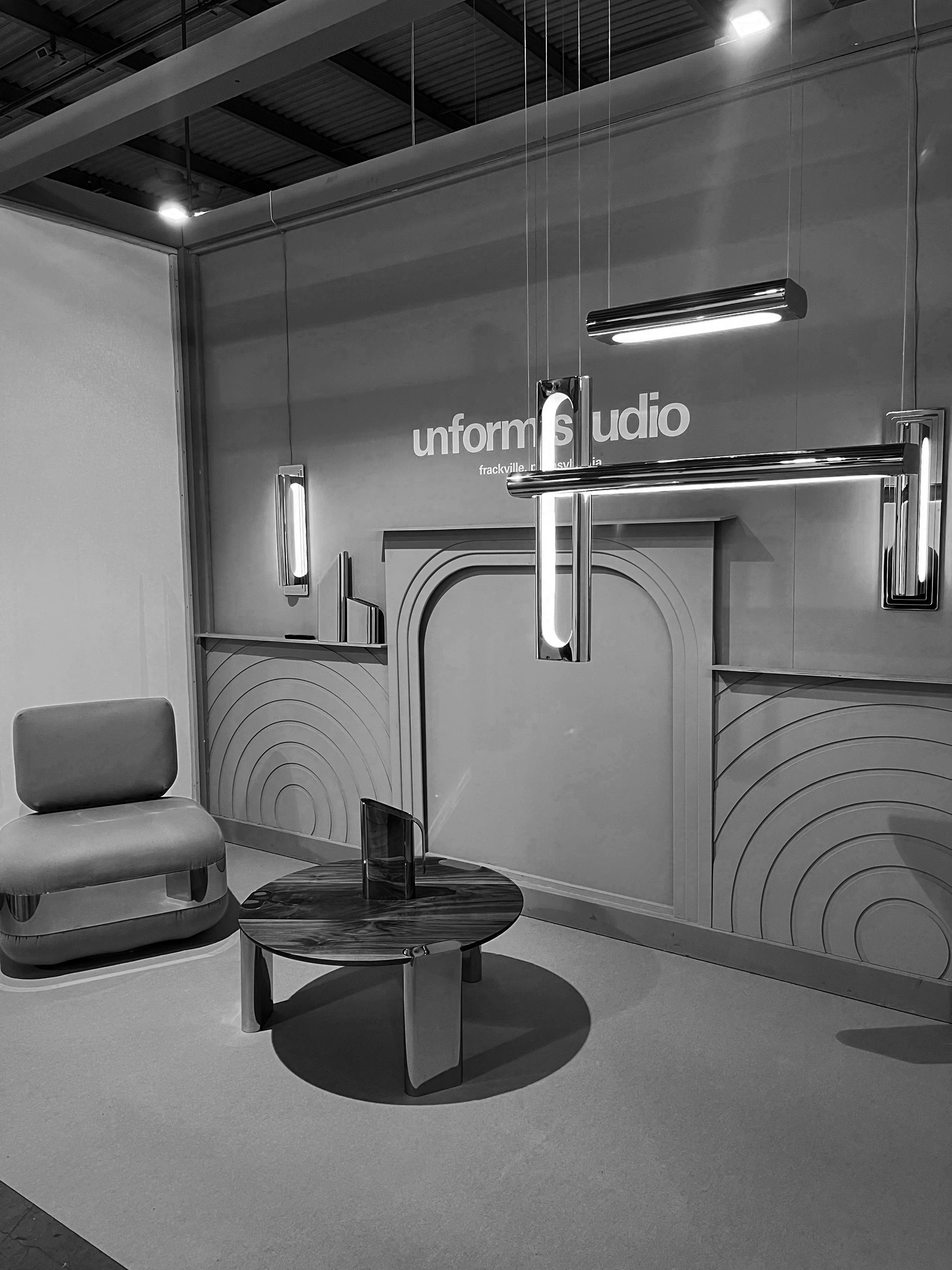 Modern interior space with a chair, a small round table, and decorative lighting fixtures, with text on the wall reading 'uniform studio'.