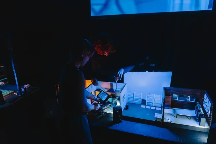 Two people working with a detailed miniature architectural model in a dark room with blue lighting.