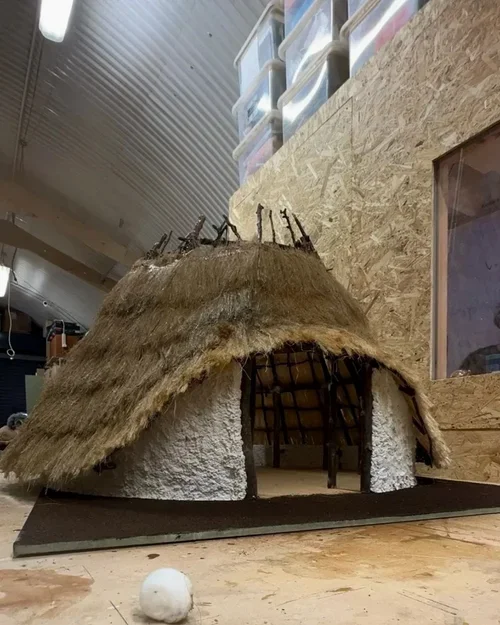 Model of a traditional round hut with a thatched roof and white textured walls, placed on a flat surface indoors.