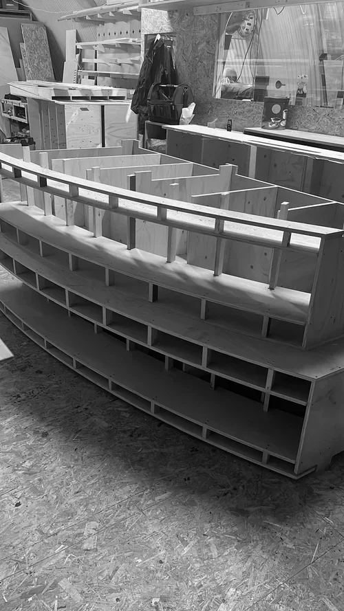 Wooden bar or countertop structure with multiple shelves underneath in a workshop.