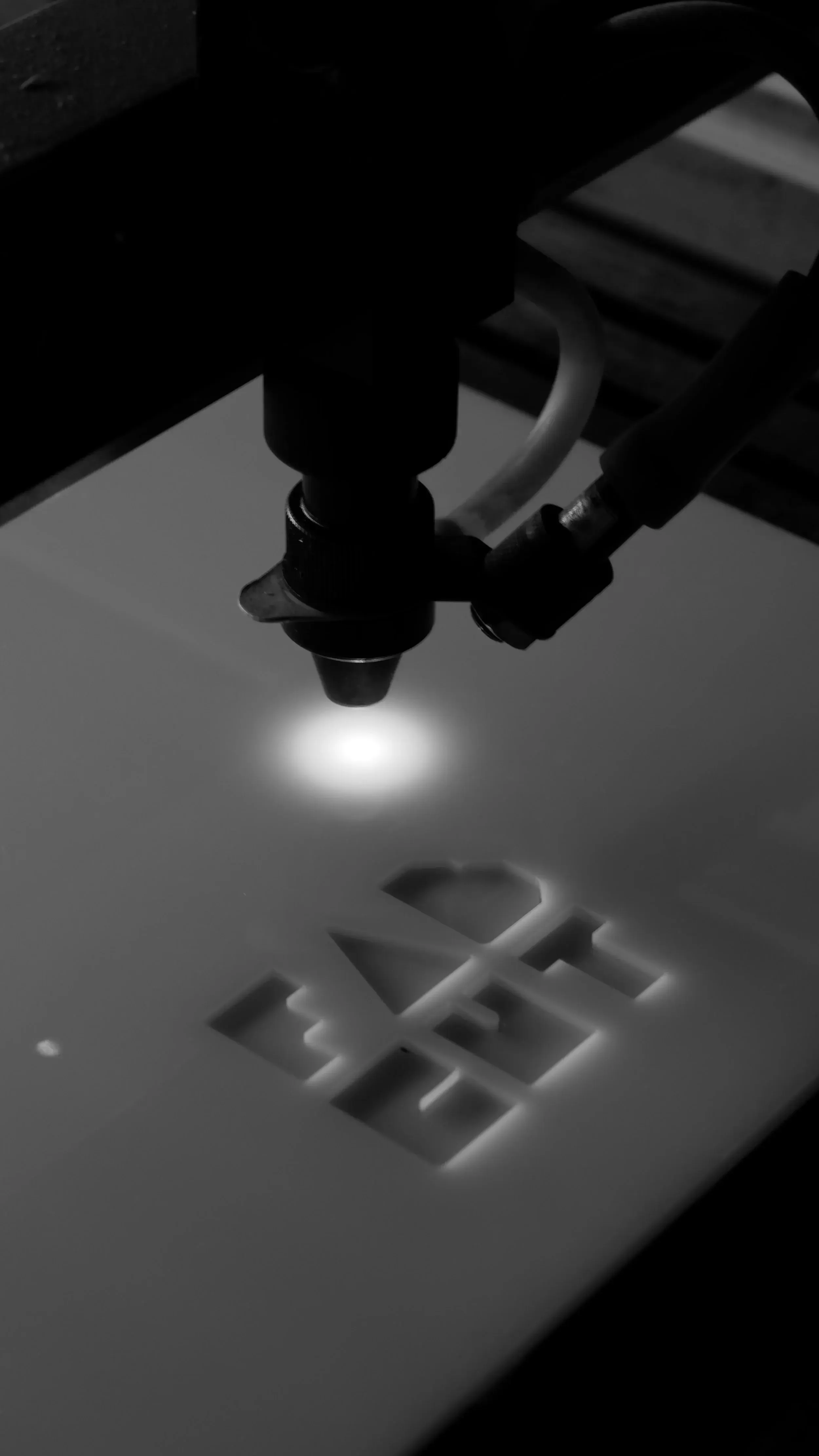 Close-up of a laser cutting machine directing a focused laser beam at a white sheet of material, with visible grid pattern beneath.