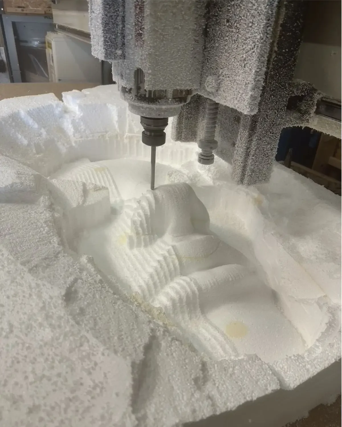 Close-up of a CNC machine carving detailed patterns into a white foam block.