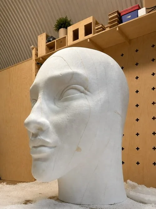 A large white sculpture of a human head on display in an indoor setting.