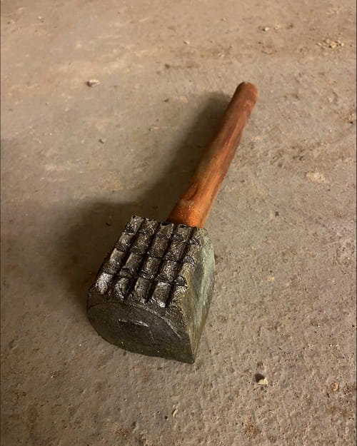 A metal hammer with a wooden handle resting on a concrete floor.