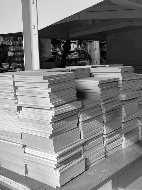 Stacks of blank white posters or boards stacked on a wooden table in a warehouse or printing facility.