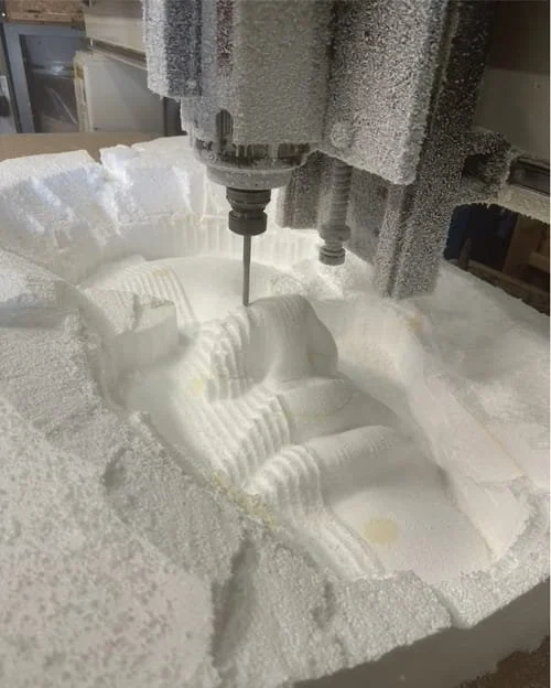 A CNC machine carving a detailed sculpture or pattern into a block of white foam.