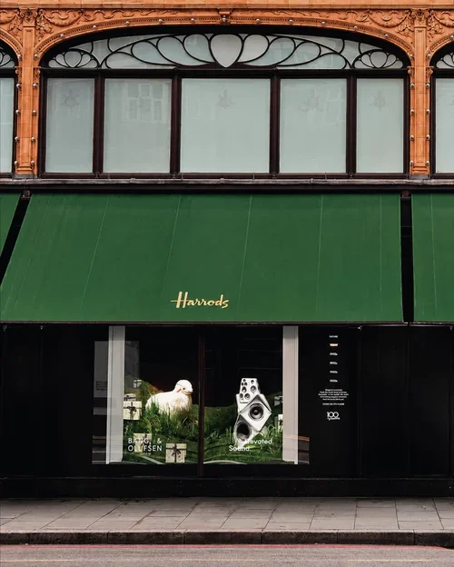 Harrods storefront with a green awning, windows above, and a display window with a sheep and speakers inside.
