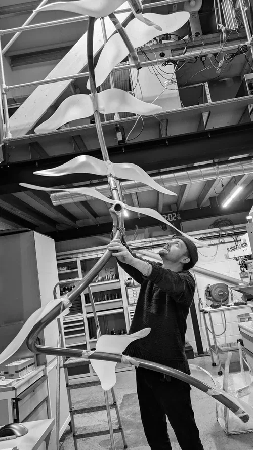 A man working on assembling a mechanical sculpture with large, abstract, wing-like components in a workshop.
