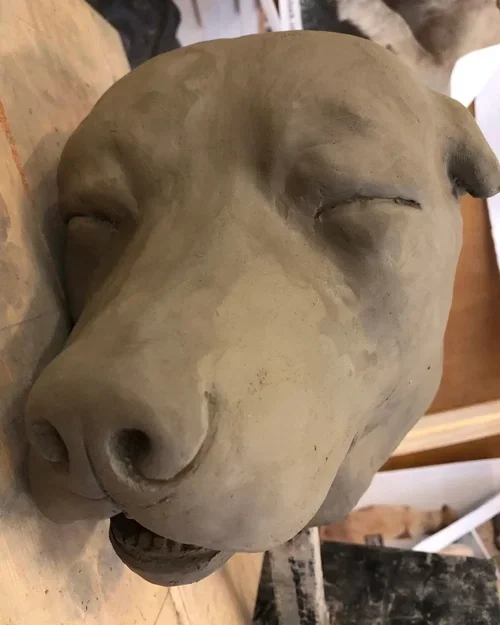 Clay sculpture of a dog's head with closed eyes, on a wooden surface.