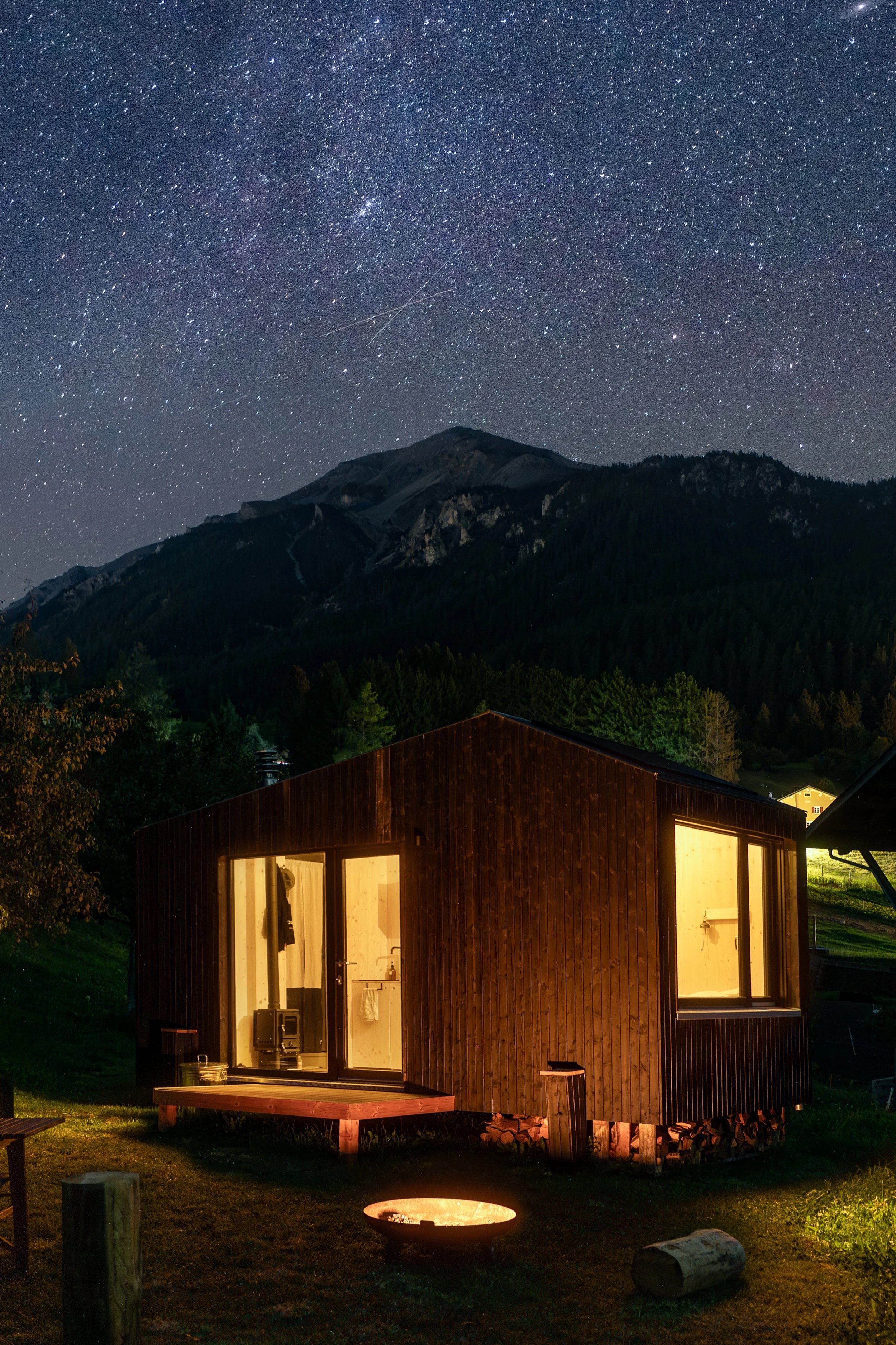 Ein Holzhaus bei Nacht unter einem sternklaren Himmel mit Bergen im Hintergrund